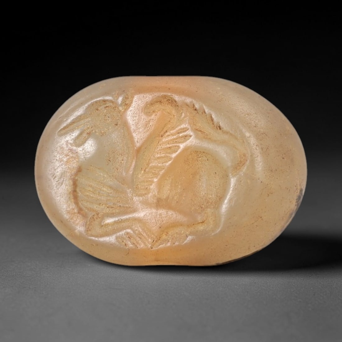 Ancient Near Eastern Chalcedony Hemispherical Stamp Seal - Griffin Motif Artifact, 93AM: This artifact is a hemispherical chalcedony stamp seal, executed in the classic glyptic tradition of the ancient Near East. The face features a dynamic griffin (a winged lion composite) in striding po