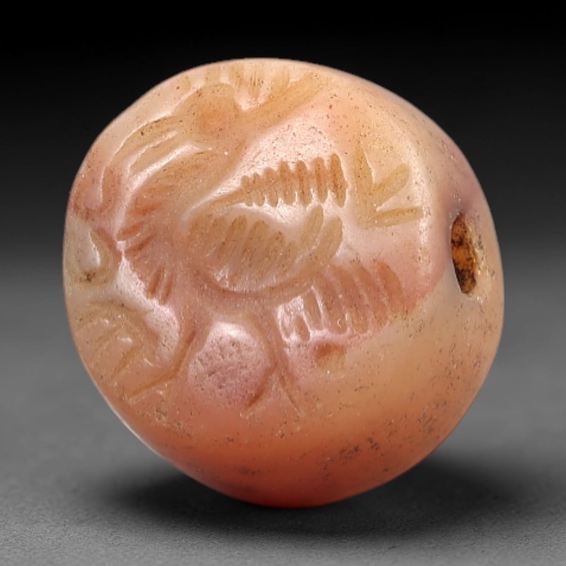 Ancient Carnelian Intaglio - Near Eastern Bird Amulet, 25AL: Crafted from carnelian, this spherical bead amulet bears a shallow incised depiction of a stylized bird in dynamic pose, with feathered details and linear motifs surrounding the figure. A suspension h