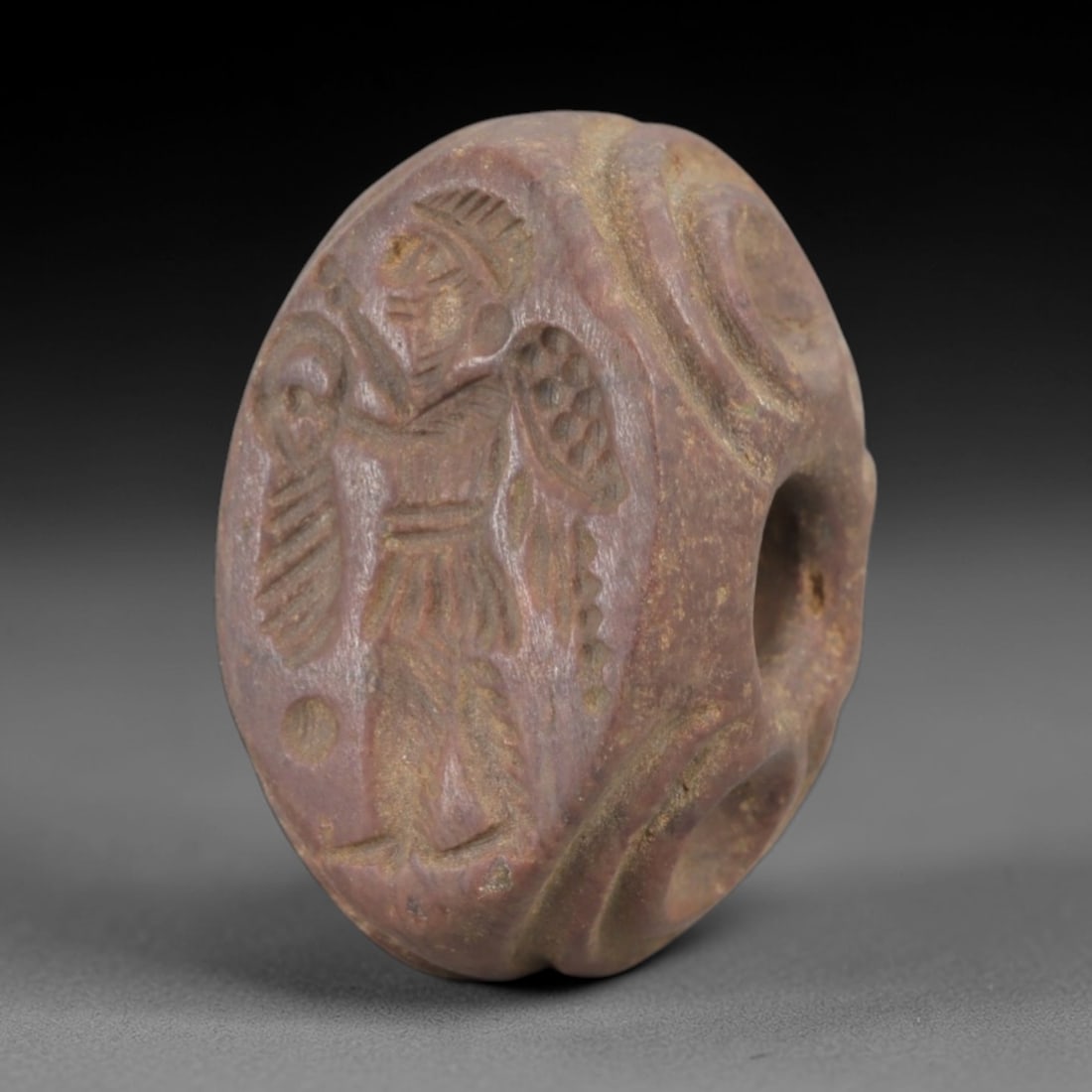 Ancient Steatite Stamp Seal - Sasanian Warrior, 73AK: Carved from steatite, this hemispherical Sasanian stamp seal features a central standing warrior motif, clad in a crested helmet and short tunic, wielding a weapon and shield, consistent with Sasanian