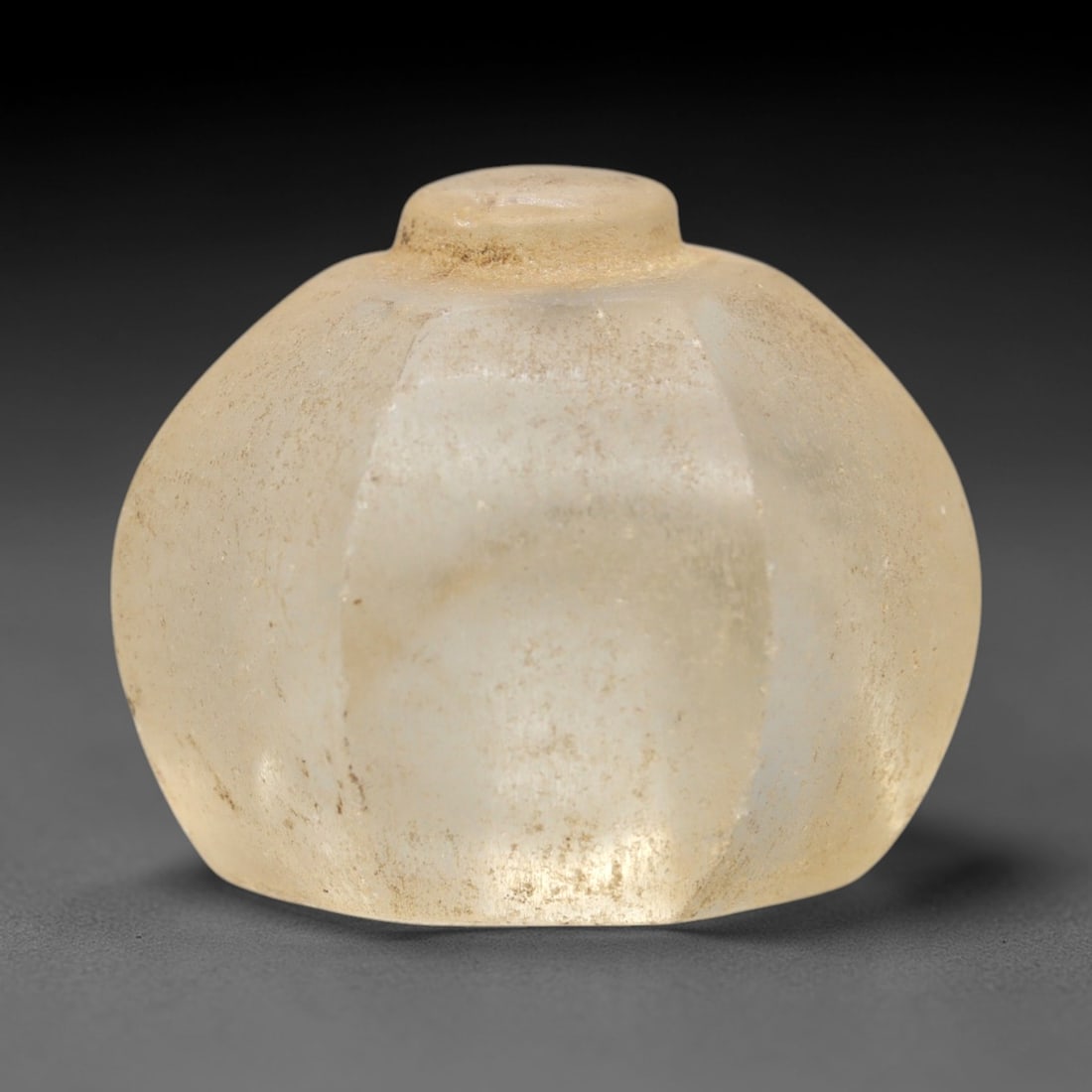 Ancient Glass Relic - Medieval Egyptian Faceted Object, 77ZR: Crafted from translucent pale glass with earthy encrustations, this bulbous relic features a faceted body and a small domed knob at the apex, reflecting medieval Egyptian glassworking traditions. The