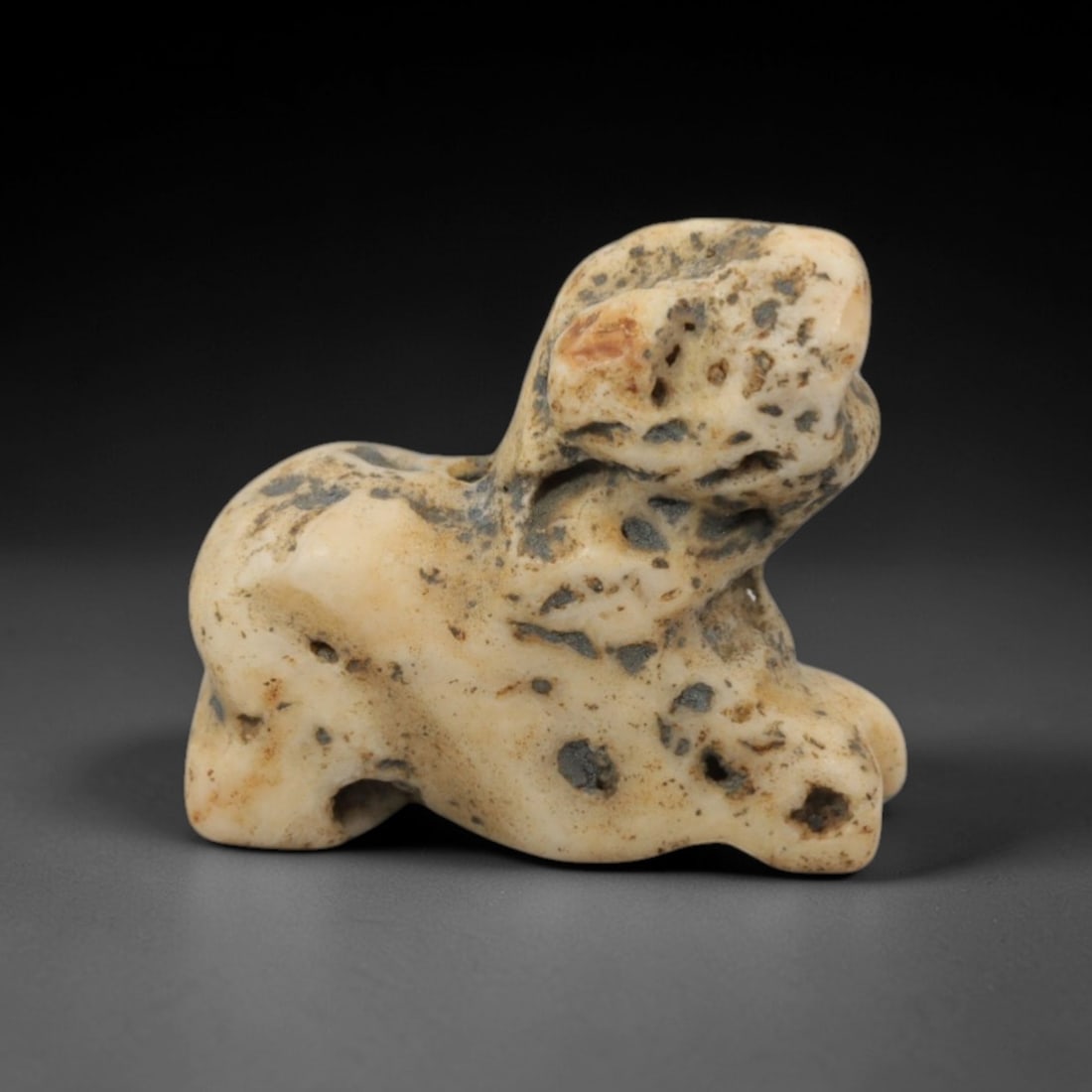 Ancient Cream Stone Recumbent Animal Amulet - Near Eastern Miniature Figurine, 11XQ: Carved from a creamy-white stone with natural grey and brown mineral inclusions, this charming amulet depicts a stylized recumbent animal, likely a feline or small ungulate, a classic motif in ancient