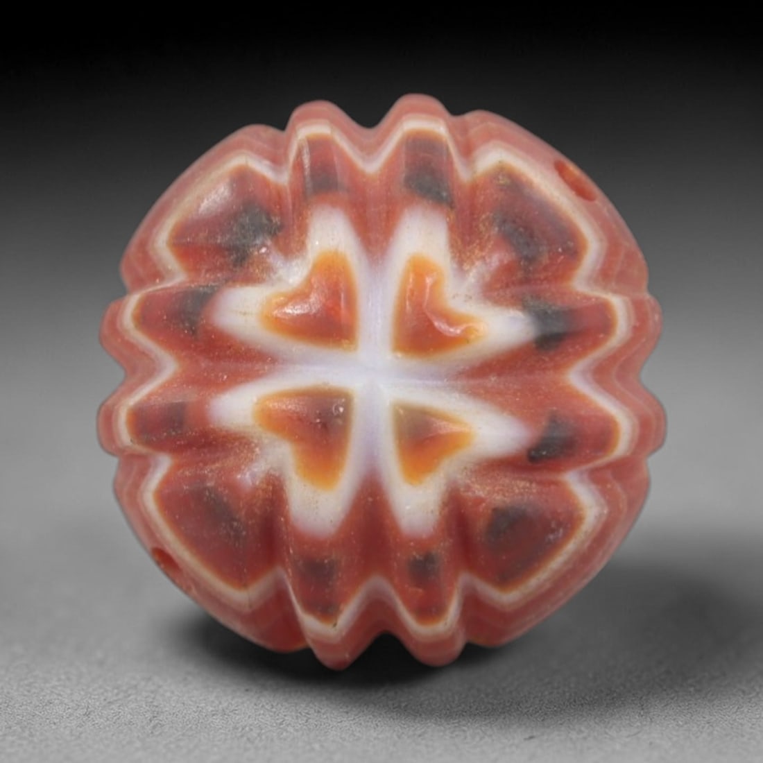 Antique Agate Walnut Bead - Central Asian Carved Gemstone, 1AR: Carved from banded agate with a rich red base and creamy white-orange inclusions, this bead features a deeply ridged, walnut-like form with a central cross pattern of four raised heart-shaped motifs.