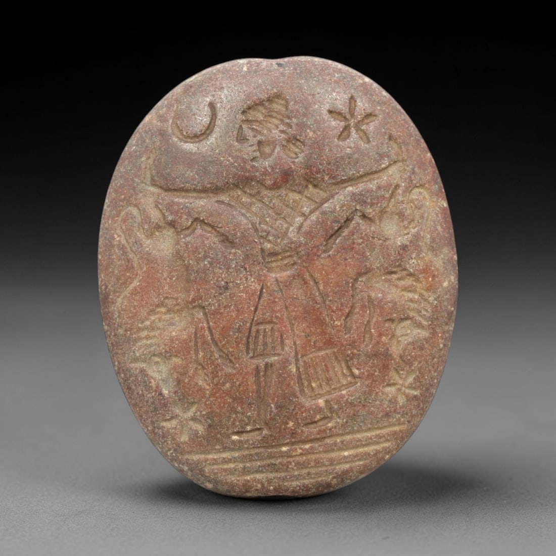 Ancient Stone Intaglio Bead - Near Eastern Winged Deity Figure, 79ZR: Carved from a reddish-brown stone, this oval intaglio bead depicts a winged anthropomorphic deity in raised relief, flanked by celestial motifs including a crescent moon and star forms, consistent wit