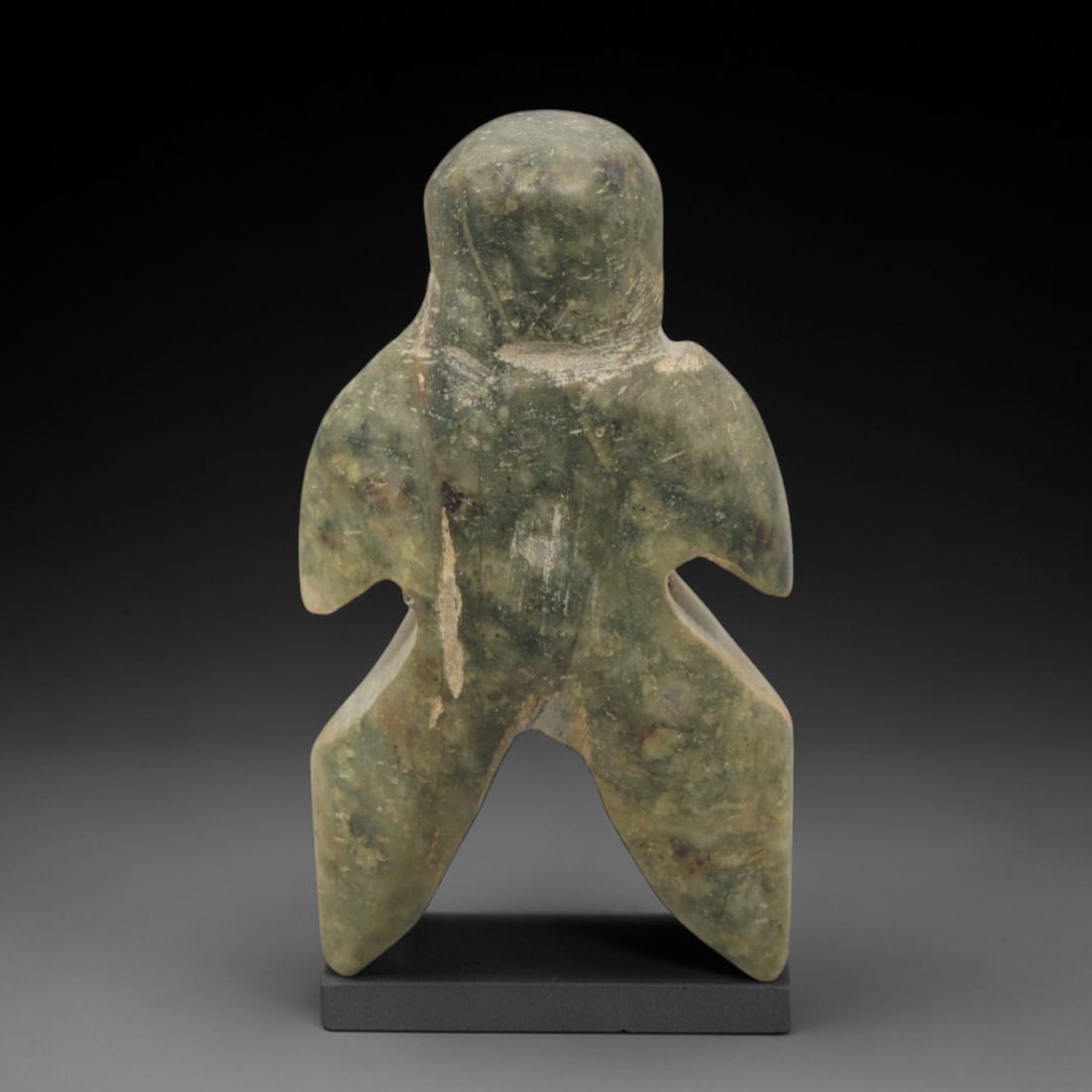 Ancient Stone Anthropomorphic Figurine - Near Eastern Idol, 50XR: Carved from mottled green stone, this stylized anthropomorphic figurine features a rounded head, broad wing-like arms, and angular, splayed legs. The geometric, abstract design is characteristic of An