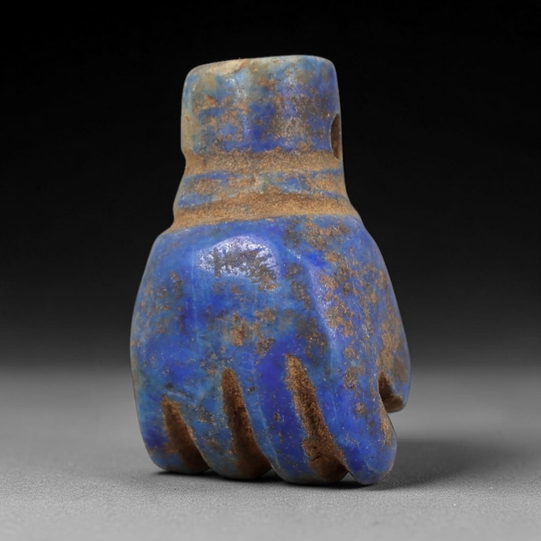 Ancient Lapis Lazuli Fist Amulet - Egyptian Ritual Pendant, 13AP: Carved from lapis lazuli, this amulet is formed in the shape of a clenched fist, with incised lines delineating the fingers and a horizontal band encircling the wrist-like upper section. The deep blue