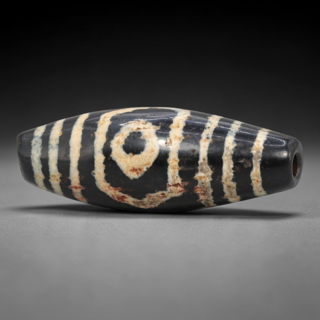 Ancient Agate 3-Eye Dzi Bead - Himalayan Amulet, 68XV: Crafted from dark translucent agate, this bead features three etched circular eye motifs flanked by parallel linear bands, executed in the traditional Himalayan Dzi bead technique. The form is an elon