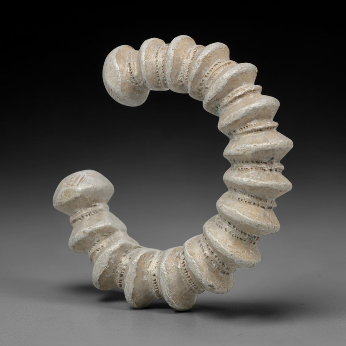 An African Silvered Aluminium Bracelet, 20th Century, 97FT: Formed from silvered aluminium, the bracelet is constructed as an open C-shape, composed of a series of stacked, disc-like segments separated by fine, incised linear bands. The terminals are rounded a