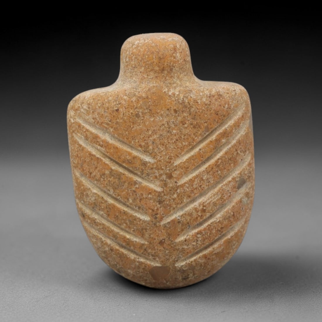 Ancient Limestone Leaf Amulet - Near Eastern Pendant, 65ZW: This amulet is carved from warm tan limestone, shaped as a rounded shield-like form with a short cylindrical suspension loop at the top. Incised diagonal lines radiate symmetrically from the center to