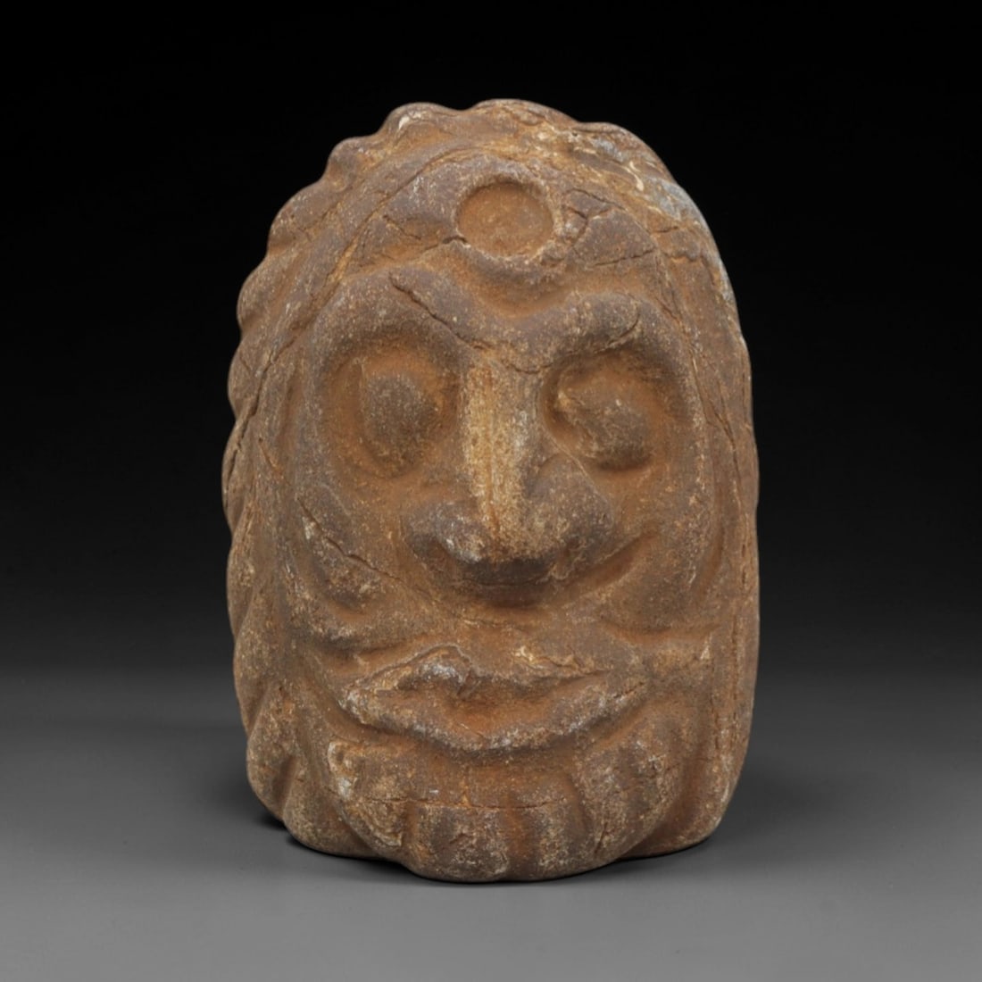 Ancient Stone Maskette - Tribal Ritual Artifact, 26FX: Carved from a coarse, earthy-brown stone with a heavily textured, weathered surface, this artifact is a diminutive maskette featuring a prominent central circular indentation above deeply recessed, al