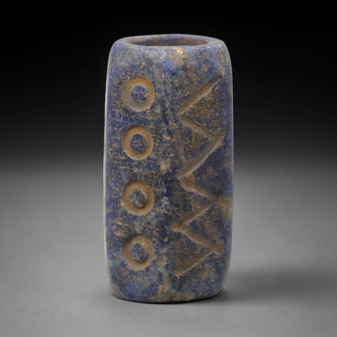 Ancient Lapis Lazuli Bead - Near Eastern Amulet, 43XV: Carved from lapis lazuli, this cylindrical bead features incised geometric decoration, with two rows of four concentric circles flanking a central band of chevron motifs, consistent with ancient Near