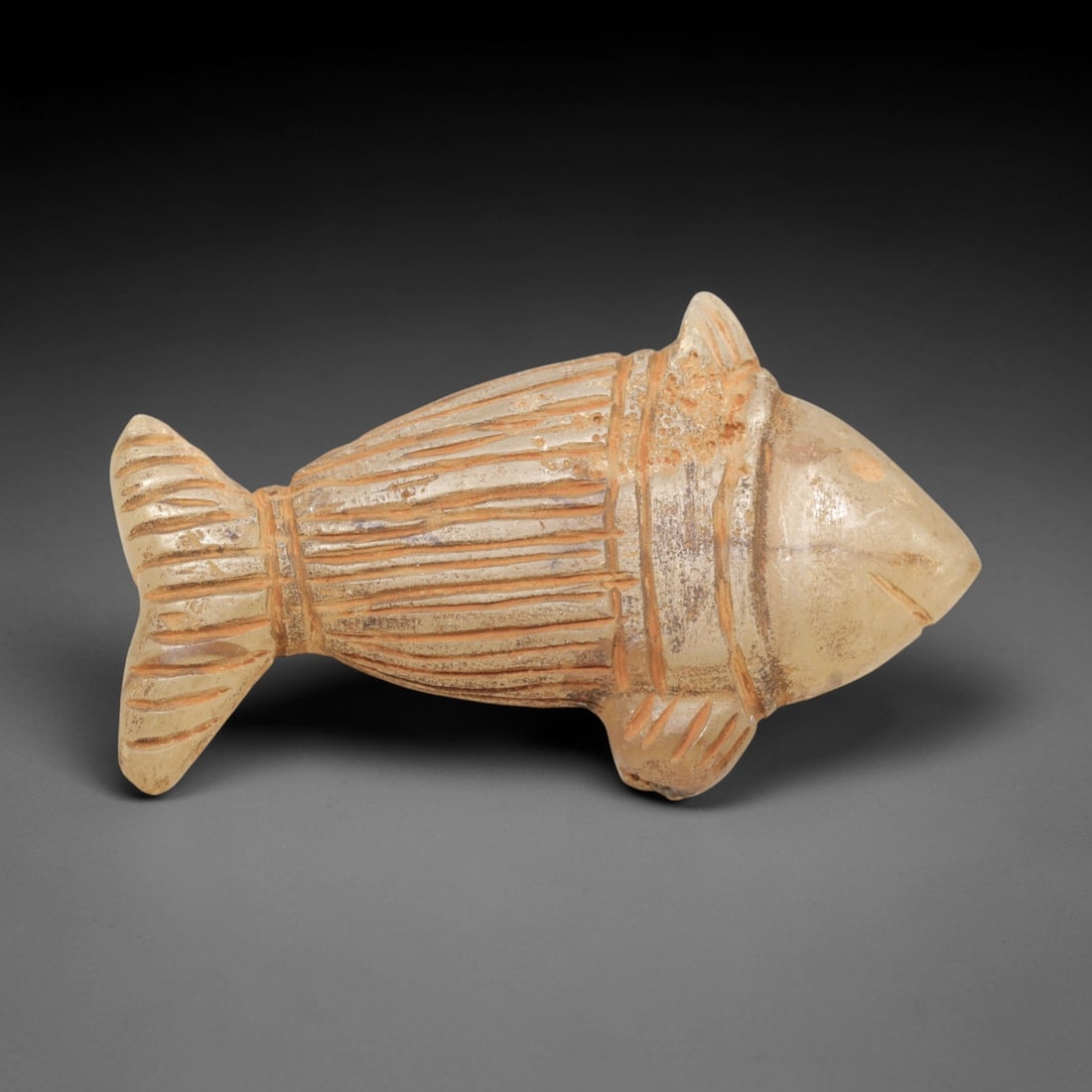 Ancient Chalcedony Fish - Zoomorphic Amulet Figurine, 64ZP: This zoomorphic amulet is carved from translucent chalcedony, shaped into a stylized fish form with incised linear details defining the segmented body, fins, and tail, alongside a small incised eye an