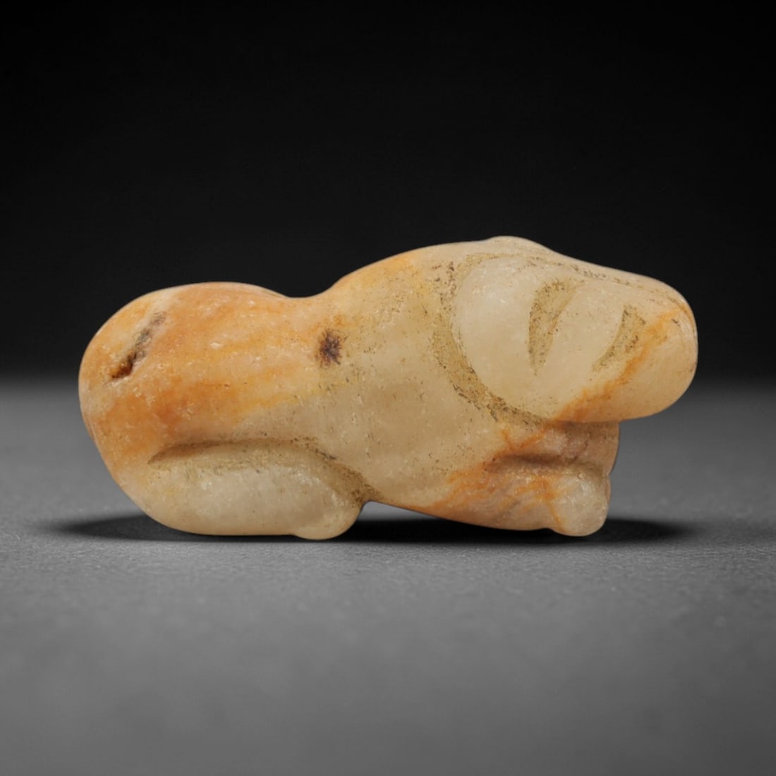 Ancient Stone Panther - Near Eastern Amulet Figurine, 34XR: Carved from pale beige stone with orange mineral veining, this amulet depicts a recumbent panther with stylized facial features, compact muscular body, and a dorsal hole drilled for suspension. The si