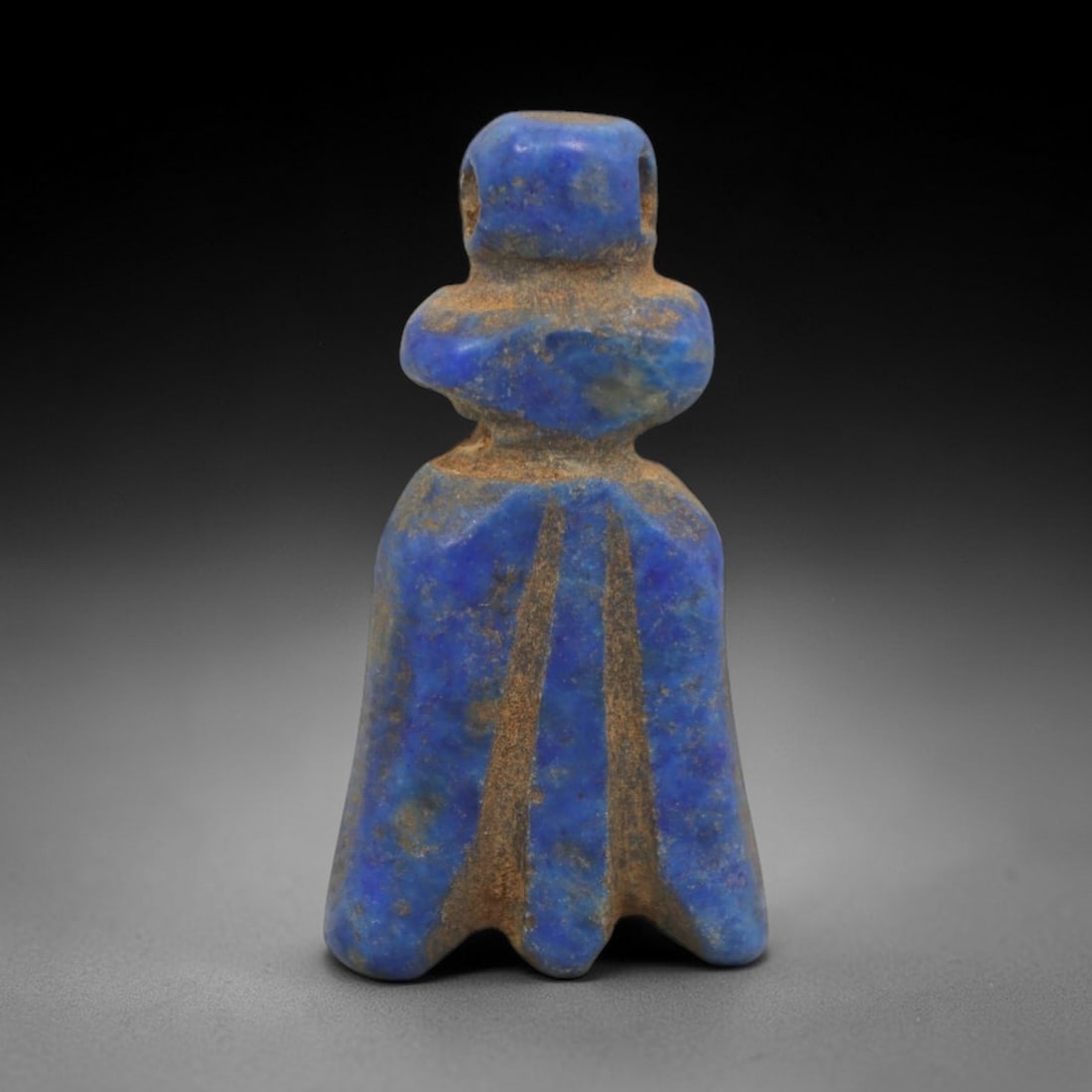 Ancient Lapis Lazuli Figure Amulet - Egyptian Ritual Pendant, 18ZT: Carved from lapis lazuli, this amulet is formed in a stylized humanoid figure with a rounded upper head pierced for suspension, a defined torso, and a flared skirt-like lower section incised with vert