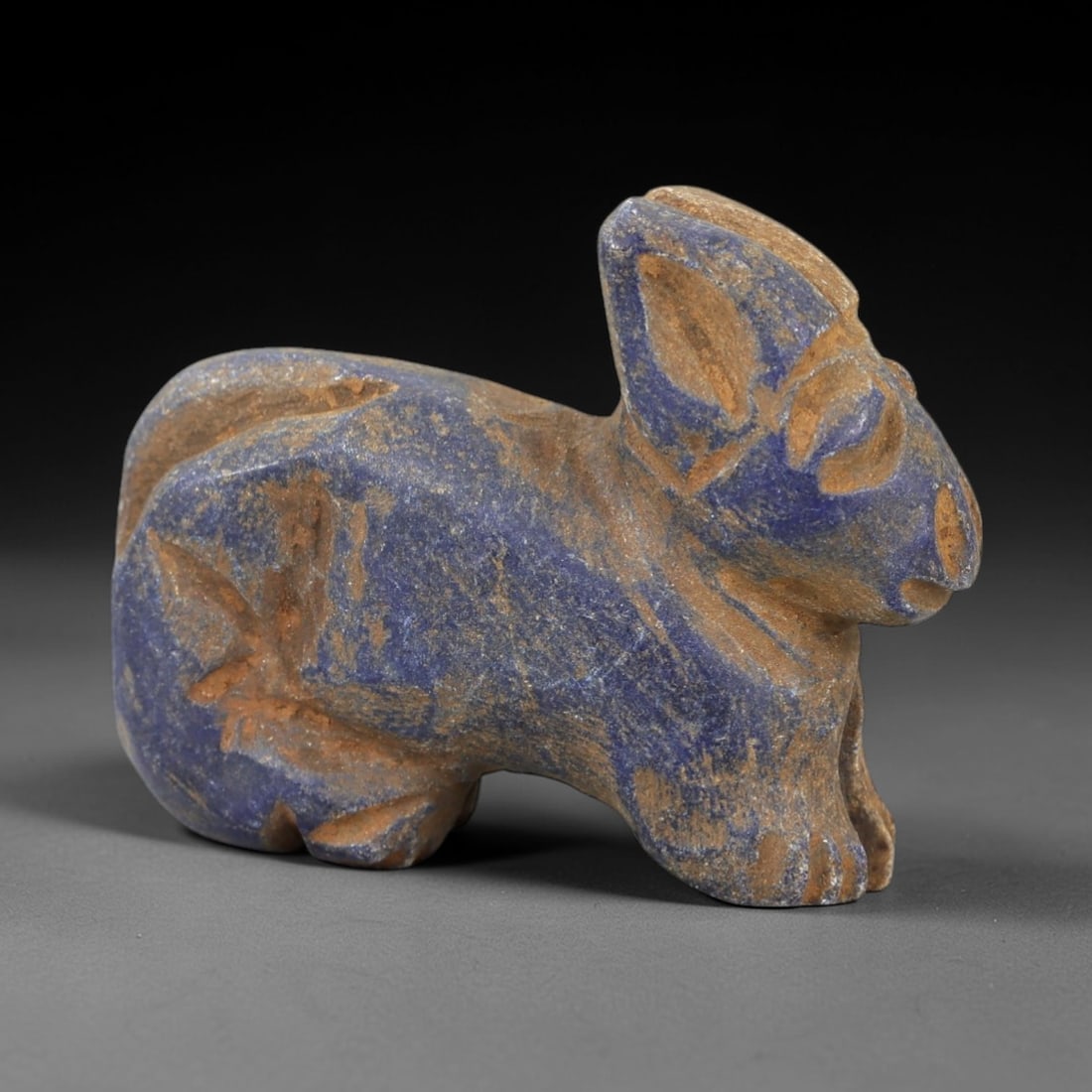 Ancient Lapis Lazuli Feline Amulet - Near Eastern Cat/Lion Talisman, 64AM: This amulet is carved from rich deep-blue lapis lazuli with natural earthy inclusions, depicting a stylized feline (cat or lion) in a recumbent, crouched posture. The piece features incised linear det