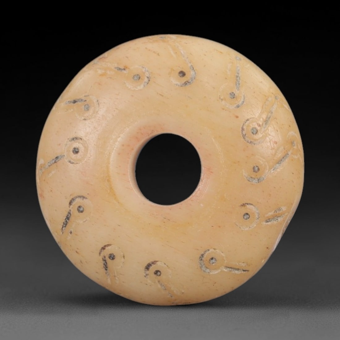 Ancient Bone Spindle Whorl - Near Eastern Dot-in-Circle Motif, 65XR: This ancient Near Eastern spindle whorl is crafted from bone, featuring incised dot-in-circle motifs encircling the central perforation. The compact, ring-like form is a traditional textile tool used