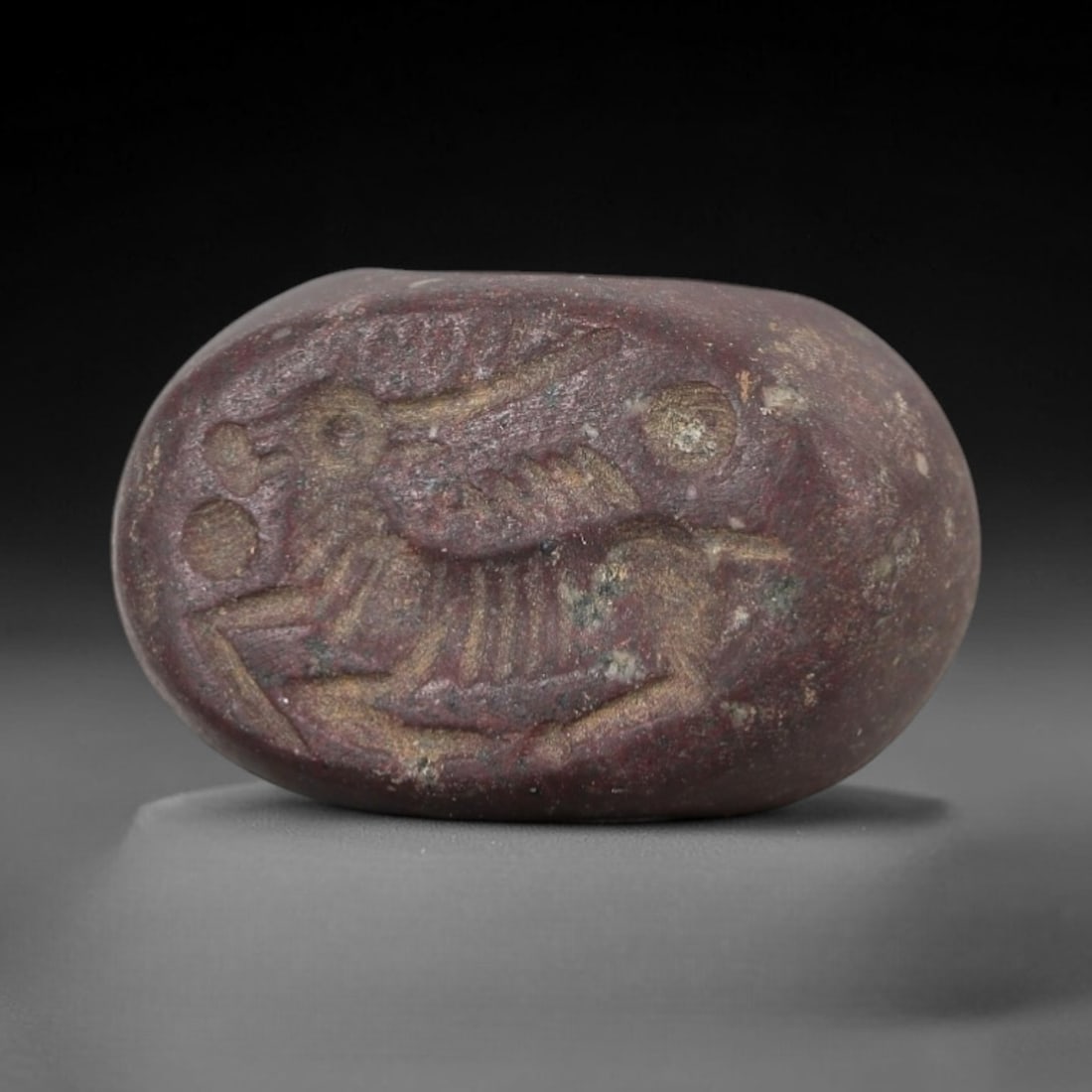 Ancient Stone Hemispherical Stamp Seal - Near Eastern Winged Stag Figure, 87AN: Carved from a dense, dark reddish-brown stone, this hemispherical stamp seal features a flat, oval face incised with a stylized winged stag in profile. The stag is rendered with prominent antlers, fea