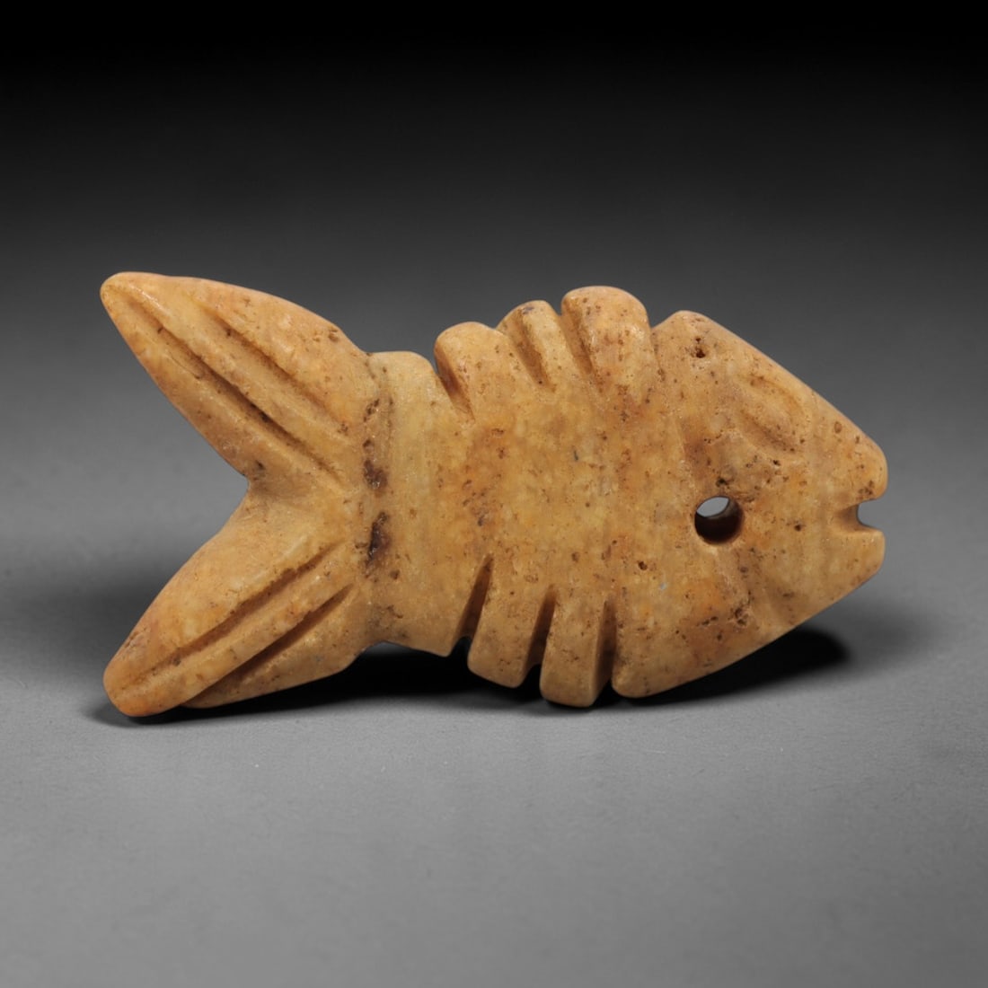 Ancient Limestone Fish Amulet - Egyptian Animal Figure, 57ZW: This amulet is carved from pale beige limestone, depicting a stylized fish with incised details defining the fins, tail, and facial features. A perforation is drilled near the head for suspension as a