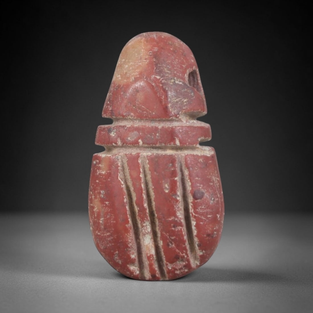 Ancient Stone Amulet - Egyptian Ritual Pendant, 74AP: This artifact is carved from variegated red stone with a weathered, earthy patina and subtle mineral inclusions, exhibiting stylized vertical linear detailing consistent with ancient Egyptian stonewor