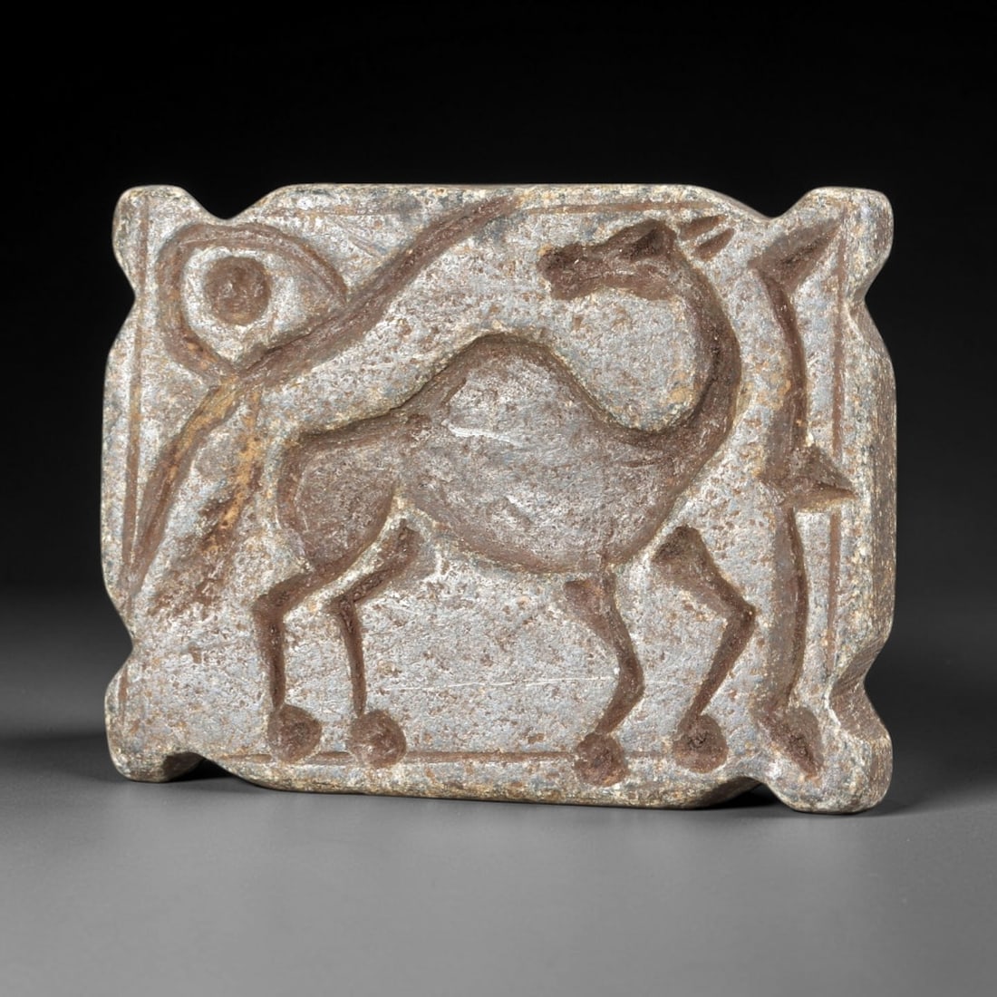 Ancient Schist Stamp Seal - Near Eastern Camel Figurine, 54AS: This ancient Near Eastern stamp seal is carved from schist, shaped as a rectangular plaque with molded and incised decoration depicting a standing camel in profile, rendered with distinct linear detai