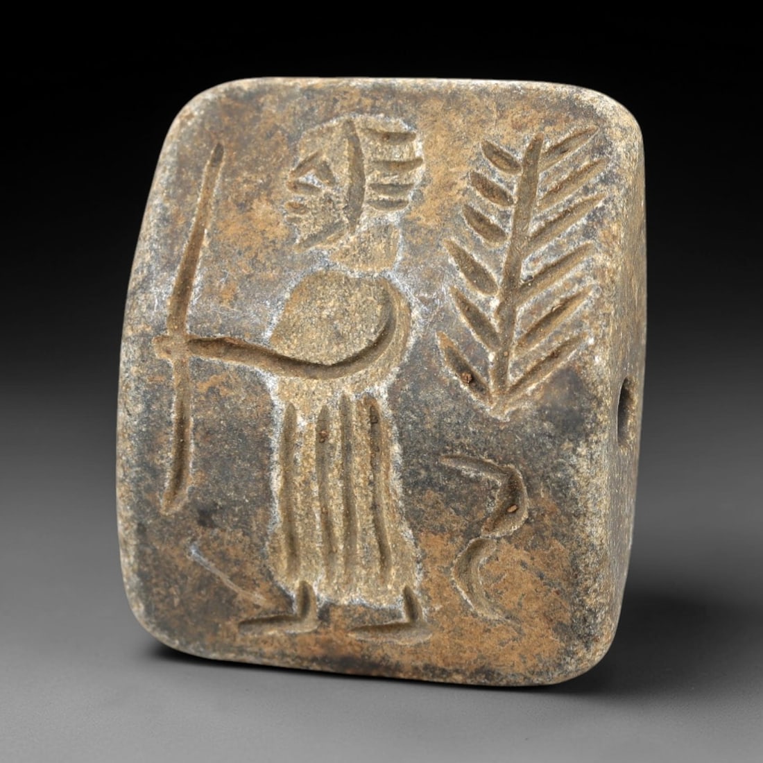 Ancient Schist Double Convex Bead Amulet - Near Eastern Figure with Tree Motif, 71AM: Carved from dark gray schist, this 3x2cm double convex bead amulet features two complementary intaglio motifs: each side depicts a standing anthropomorphic figure in profile, holding a staff or weapon