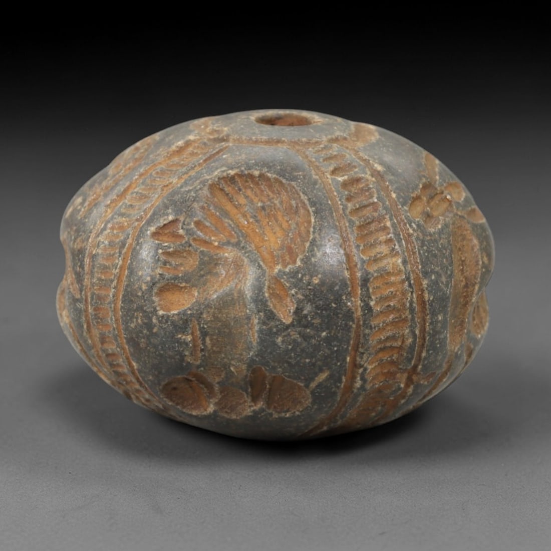 Ancient Stone Seal Bead - Near Eastern Carved Amulet, 93AK: Carved from hard stone, this seal bead features a lobed, spherical form with incised vertical bands separating panels of stylized botanical and foliate motifs, including palm fronds and floral element