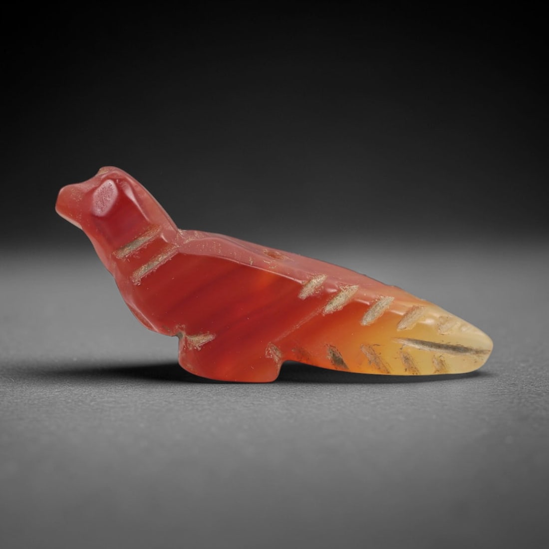 Ancient Agate Bird Amulet - Egyptian Figurine, 24AJ: Carved from banded red-and-yellow agate, this amulet is formed as a stylized recumbent bird with incised linear detailing across the neck, body, and tail to denote feather patterns. A suspension hole