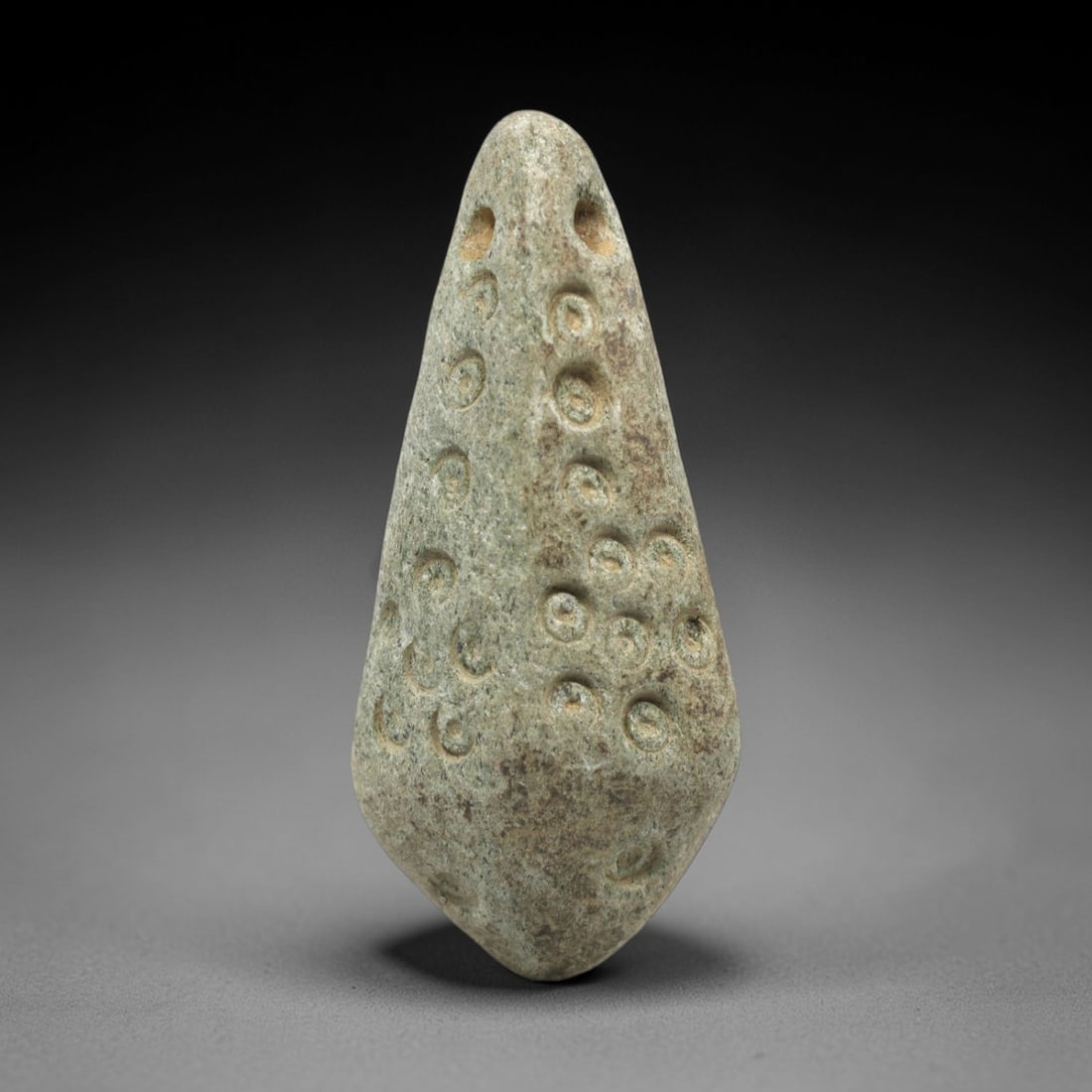 Ancient Stone Amulet - Near Eastern Spiral Motif, 58ZP: This teardrop-shaped amulet is carved from granular stone, featuring two suspension holes at the upper edge, confirming its function as a wearable talisman. The surface is decorated with multiple inci