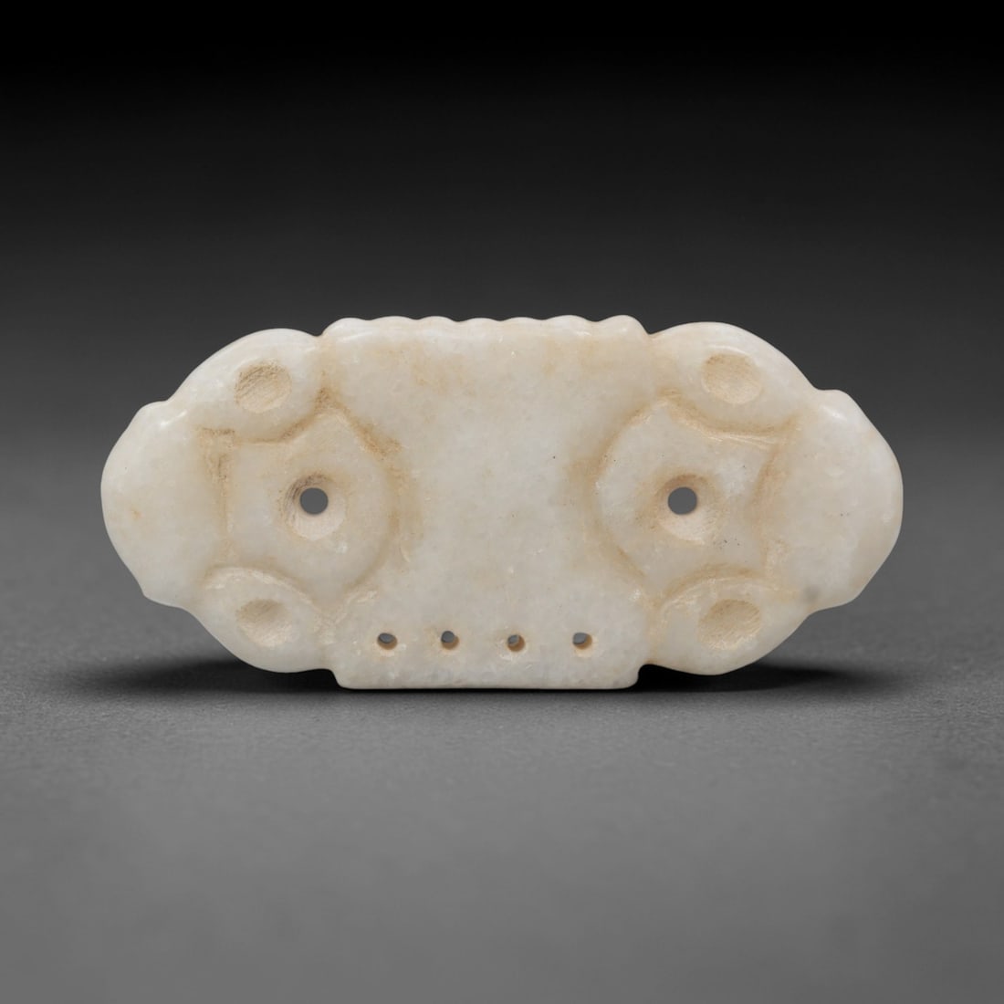 Ancient Marble Amulet Pendant - Near Eastern Ritual Relic, 99XR: Crafted from pale marble, this amulet pendant takes a symmetrical, elongated form with rounded ends. The surface is adorned with two large circular suspension holes, each surrounded by raised, stylize