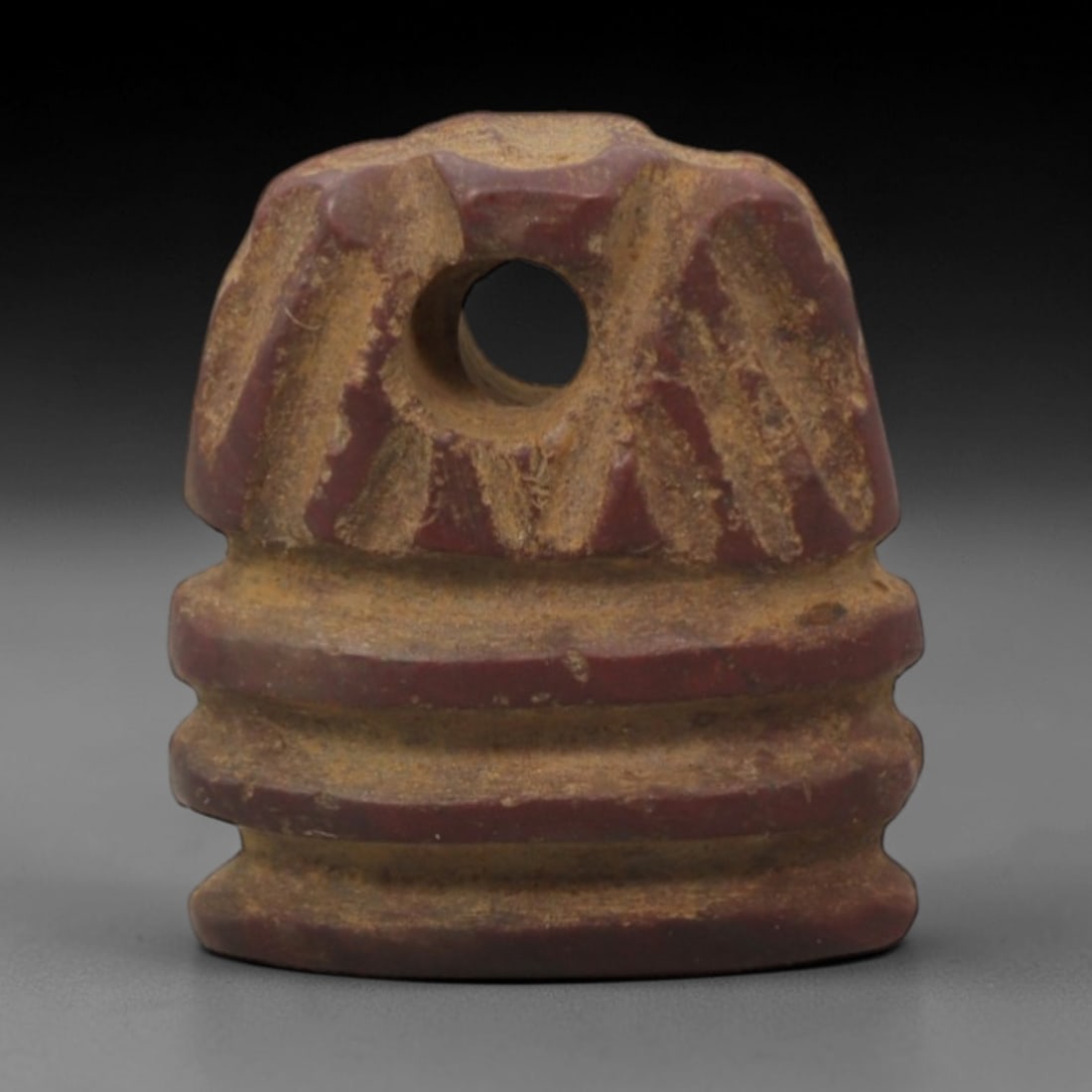 Ancient Stone Bead - Egyptian Amulet Bead, 31XR: Carved from deep reddish-brown stone, this cylindrical bead features horizontal incised ridges encircling its body and a radiating linear pattern above a central axial perforation for threading. The s