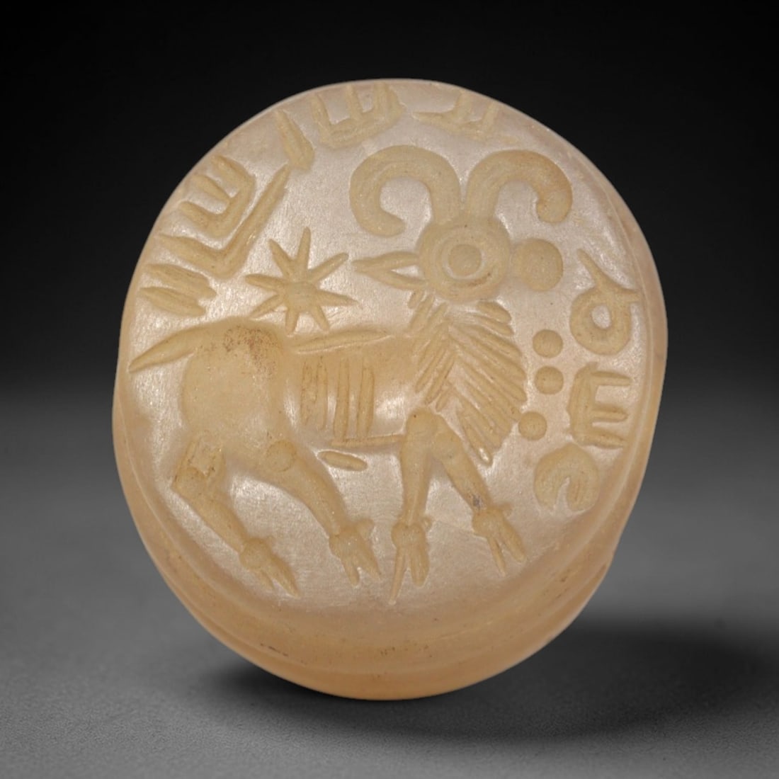 Ancient Chalcedony Hemispherical Stamp Seal - Near Eastern Ram & Celestial Script, 52ZP: Crafted from translucent, pale chalcedony, this hemispherical stamp seal bears a deeply incised depiction of a stylized ram, rendered in linear relief with distinct curved horns, patterned torso, and