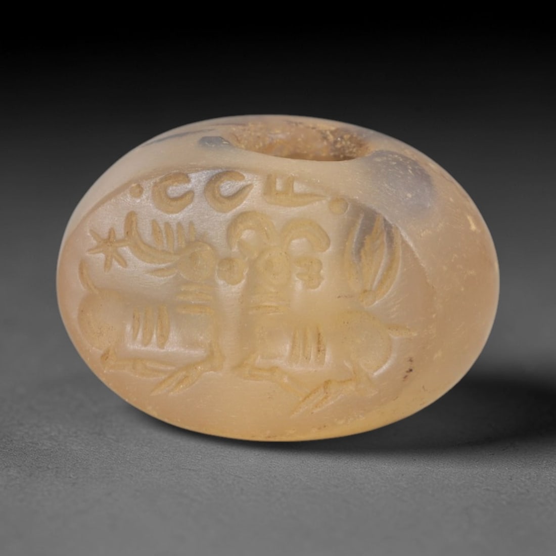 Ancient Chalcedony Stamp Seal - Sasanian Two Rams, 64AK: Carved from translucent chalcedony, this oval Sasanian stamp seal features a central composition of two stylized rams with curved horns and ribbed bodies, alongside a star motif and incised epigraphic