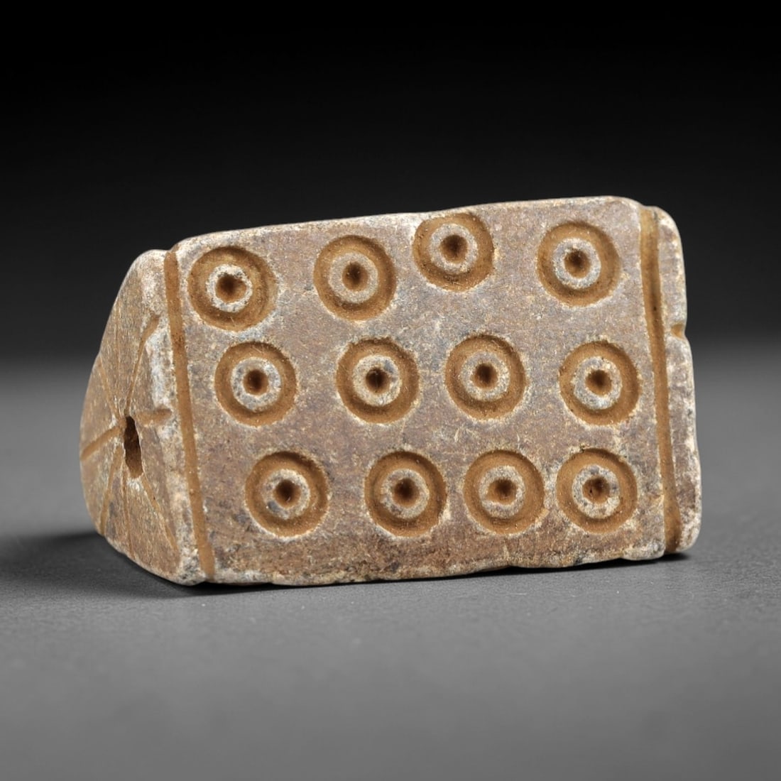 Ancient Steatite Amulet - Near Eastern Concentric Circles, 41AK: Crafted from steatite, this rectangular amulet features incised concentric circle motifs arranged in a 3x4 grid across its primary face, with radiating linear carvings surrounding the suspension hole