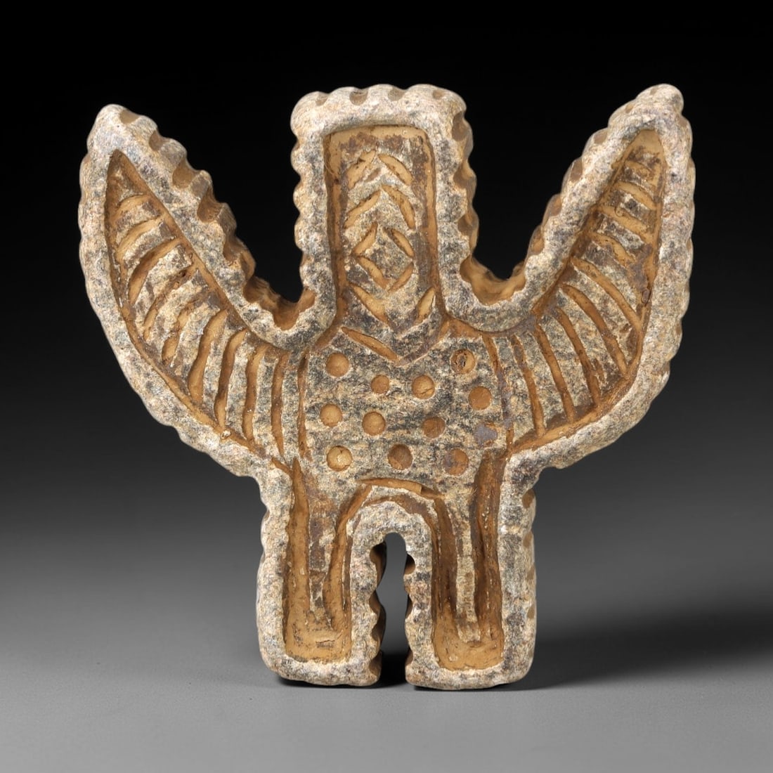Ancient Stone Anthropomorphic Amulet - Near Eastern Figure, 23AM: This amulet is carved from grey-brown stone, depicting a stylized anthropomorphic (humanoid) form with outstretched "wing-like" extensions and intricate incised detailing across the torso and limbs. T