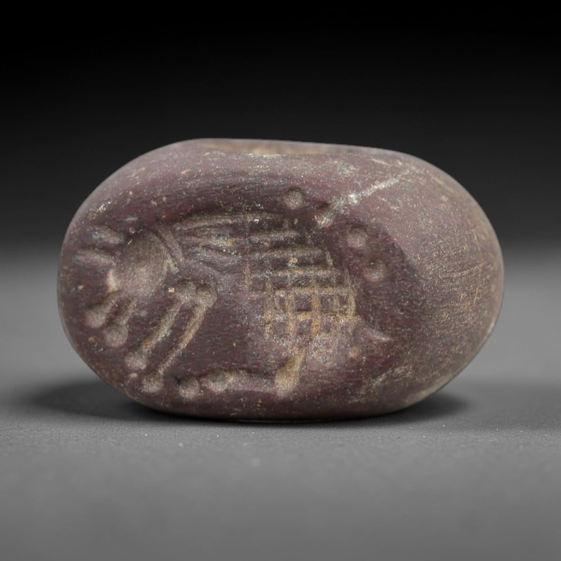 Ancient Stone Hemispherical Stamp Seal - Near Eastern Zoomorphic Figure, 26AN: Carved from a dense, dark reddish-brown stone, this hemispherical stamp seal features a flat, oval face incised with a stylized zoomorphic creature alongside a radiate sun motif. The creature is rende