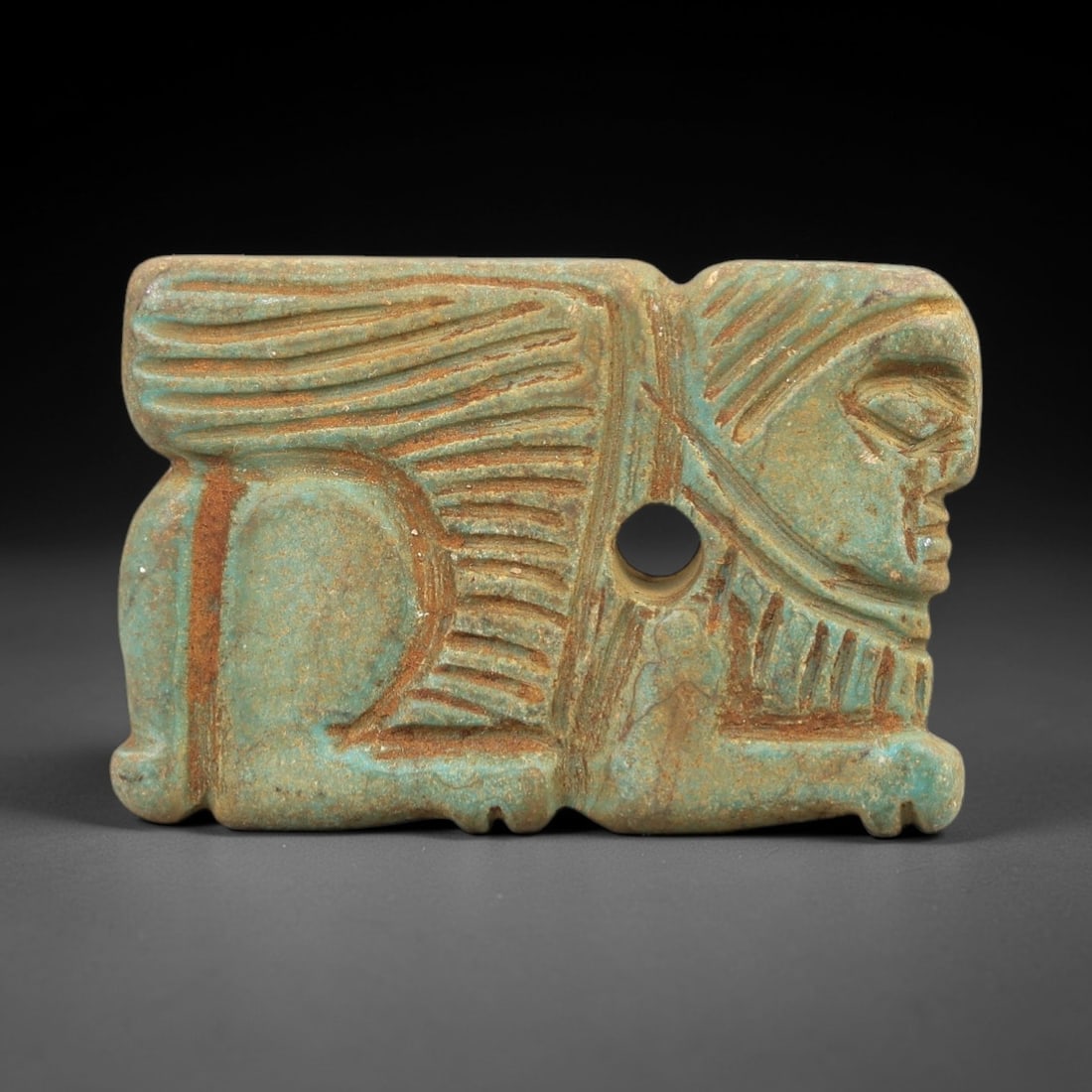 Ancient Turquoise Sphinx Plaque Amulet - Near Eastern Ritual Pendant, 44AN: Carved from turquoise, this plaque amulet depicts a recumbent sphinx with a human face, stylized headdress, and large feathered wings, featuring a central suspension hole for wearing. The vibrant turq