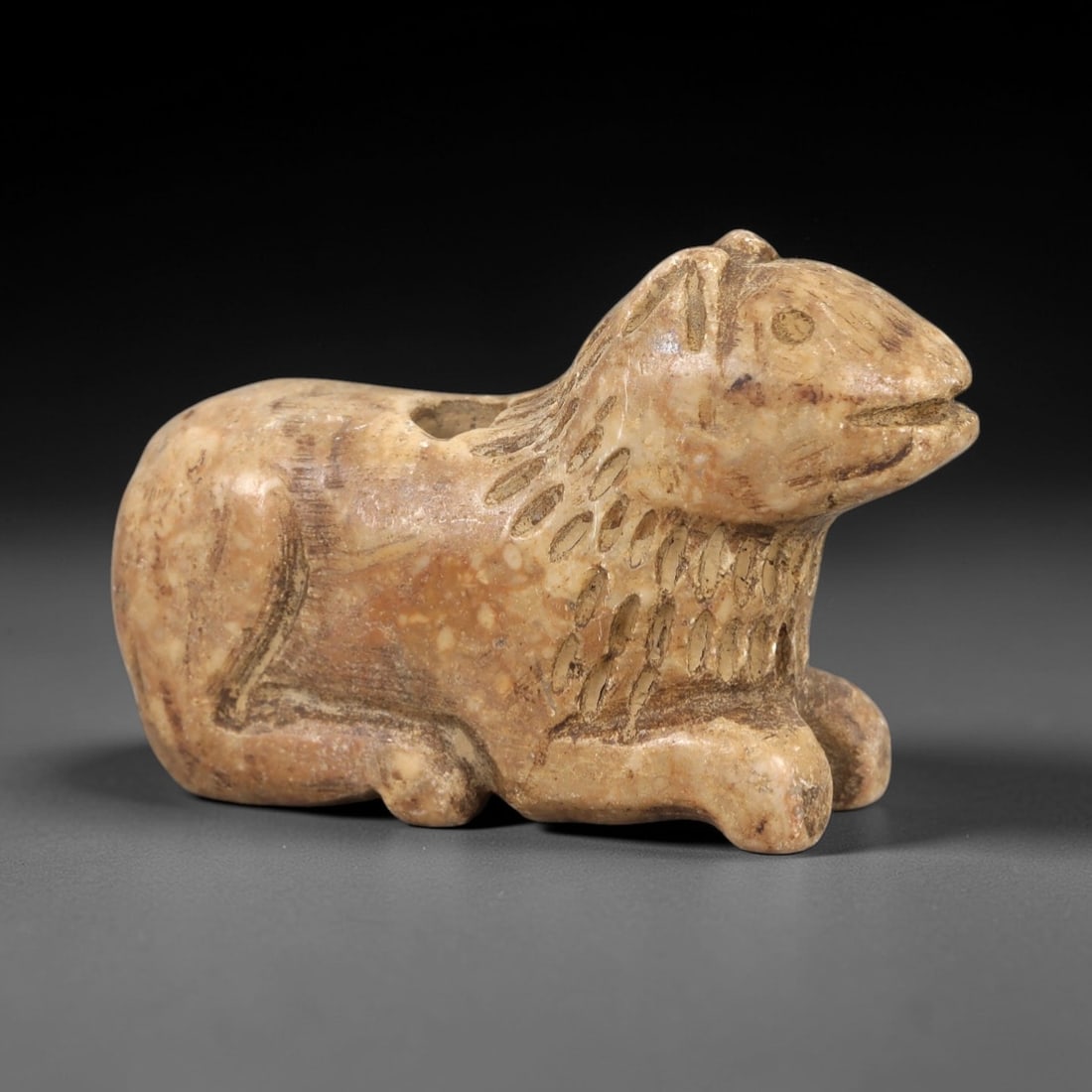 Ancient Stone Feline Amulet - Near Eastern Lion / Cat Figure, 25AM: This amulet is carved from fine speckled stone, depicting a stylized feline (lion or cat) in a compact, stylized form. Incised lines define the head, ears, body, and limbs, with a smooth, worn patina