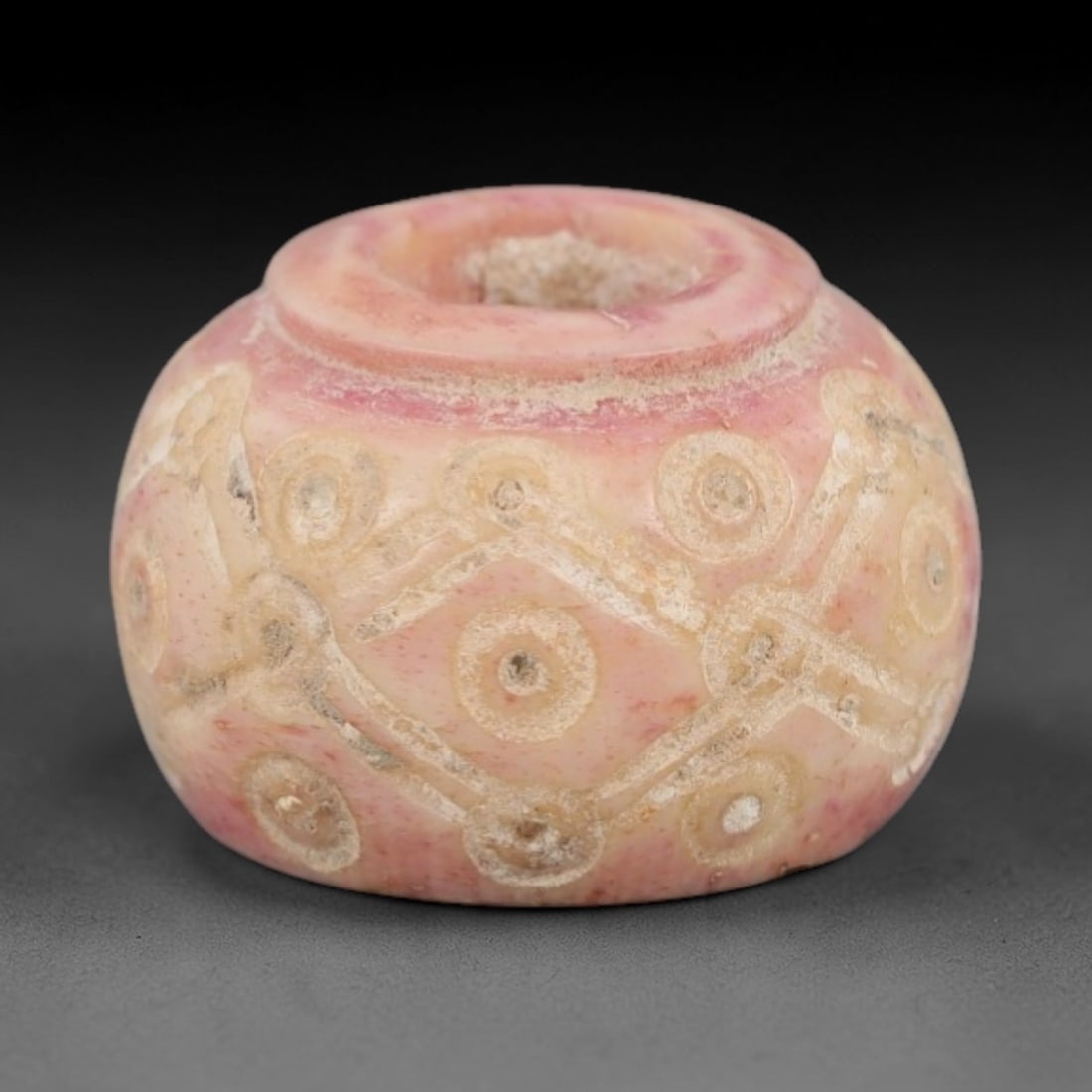 Ancient Bone Spindle Whorl - Near Eastern Interlocking Motif, 66XR: This ancient Near Eastern spindle whorl is crafted from bone, featuring a convex form with a central perforation. The surface is incised with interlocking circular and linear motifs, a decorative tech