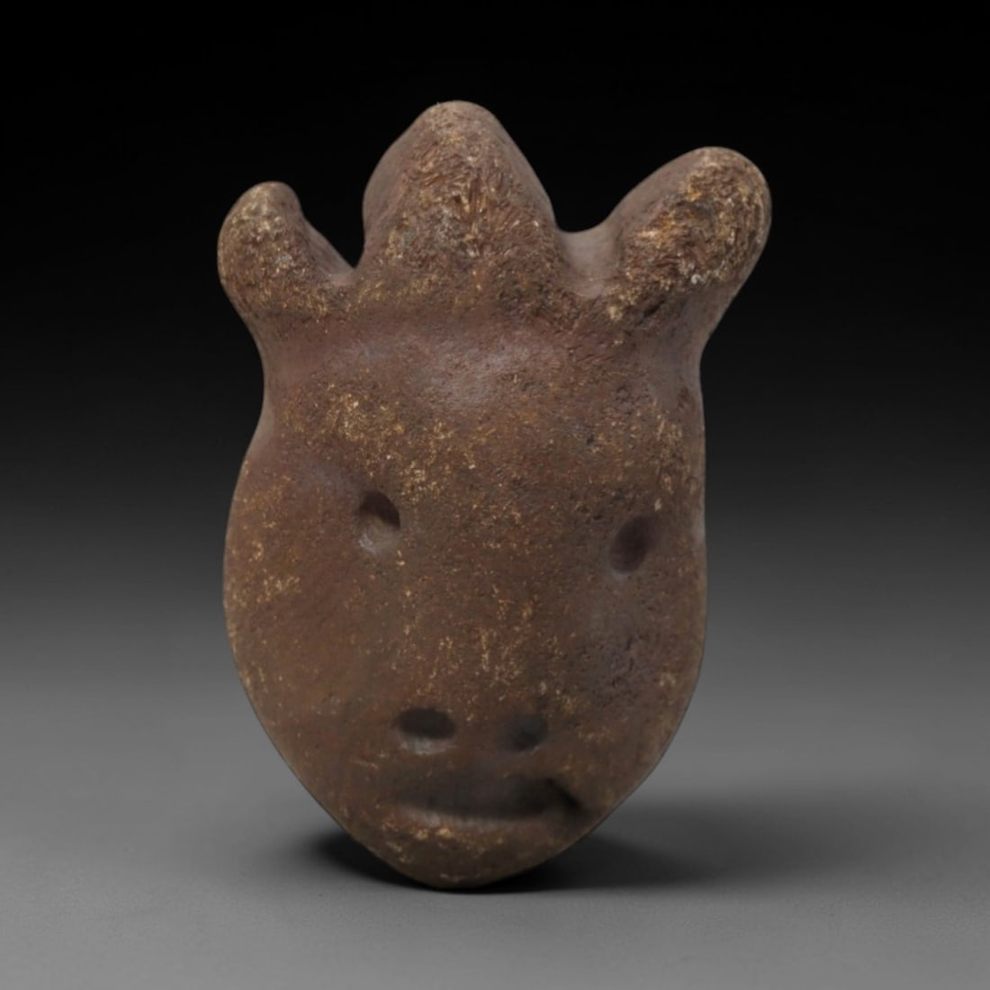 Ancient Stone Anthropomorphic Head - African Tribal Figurine, 68FW: Carved from a dense, earthy-brown stone with visible granular texture, this artifact presents a stylized anthropomorphic head crowned with three prominent, rounded horn-like protrusions. The facial fe