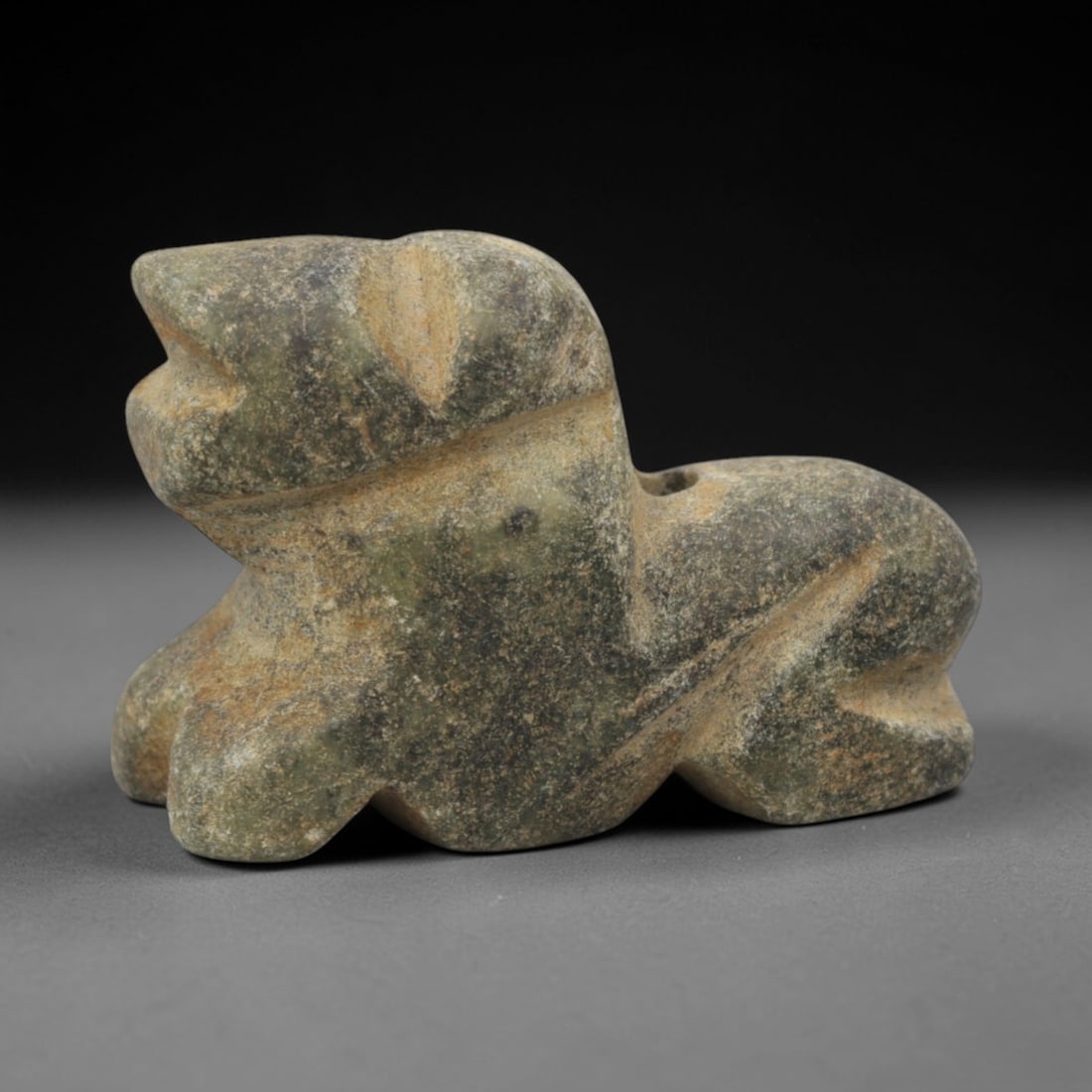 Ancient Stone Feline Amulet - Near Eastern Pendant, 45XQ: Carved from a mottled greenish-grey stone with natural earthy patination, this amulet depicts a stylized recumbent feline, likely a lion or big cat, with a blocky head, thick neck, and robust compact