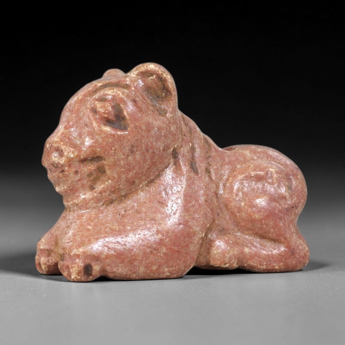 Ancient Red Stone Feline - Near Eastern Amulet Figurine, 42AS: This amulet is carved from granular red stone, exhibiting a warm, earthy patina consistent with ancient Near Eastern burial contexts. The form depicts a recumbent feline, rendered in a stylized, compa