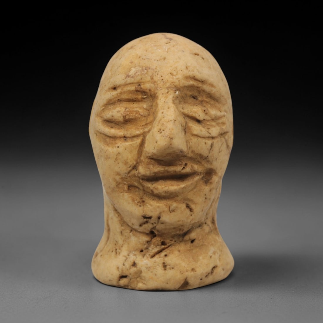 Ancient Limestone Idol Head - Bactrian Carved Figurine, 53ZQ: Carved from limestone, this ancient Bactrian idol head features a stylized human facial form with detailed eye and mouth motifs, typical of Bactrian artistic traditions. The carving exhibits moderate