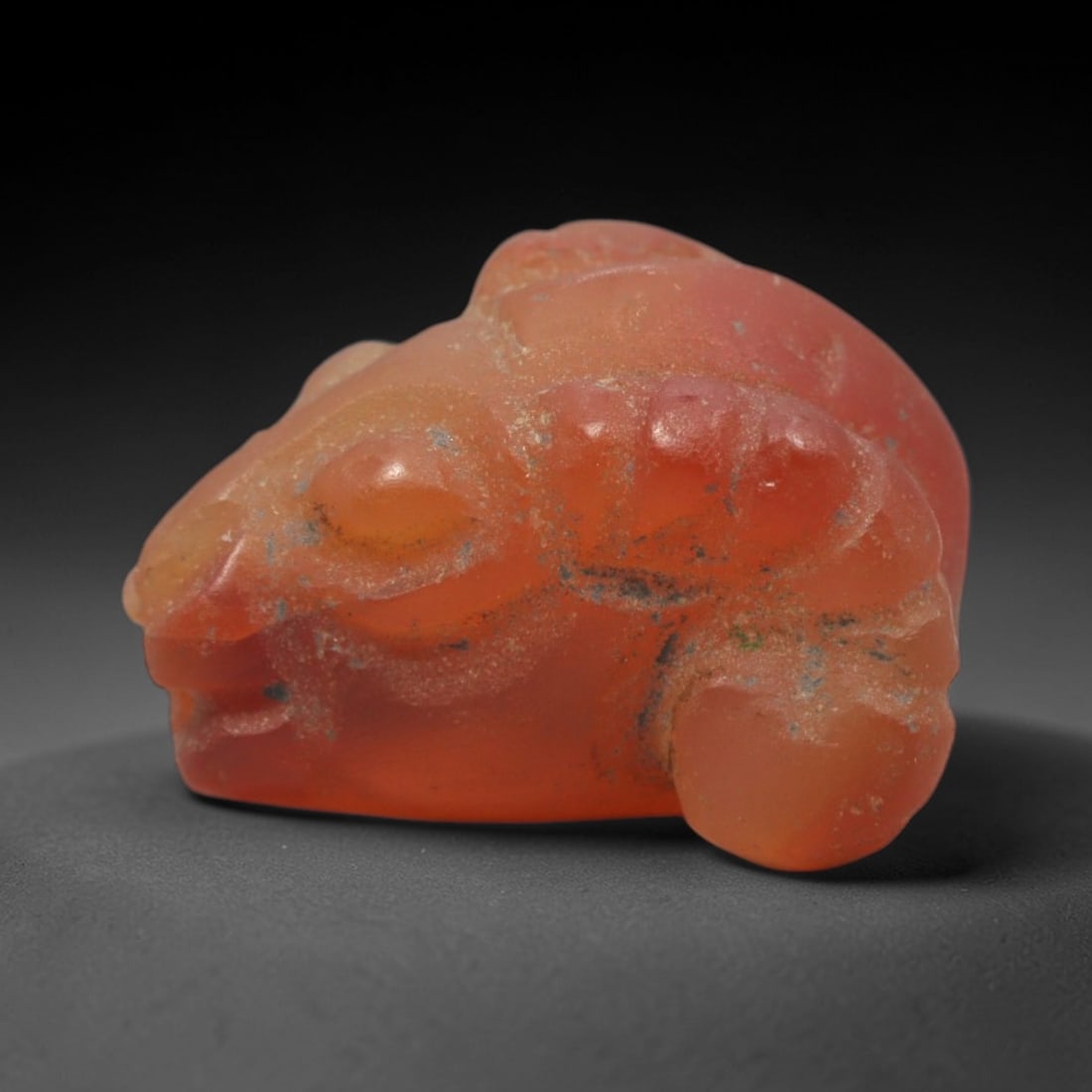 Ancient Carnelian Ram Amulet - Egyptian Figurine, 90XS: This amulet is carved from translucent orange-red carnelian, shaped into a stylized recumbent ram form with rounded anatomical detailing and subtle incisions defining facial features and horn structur