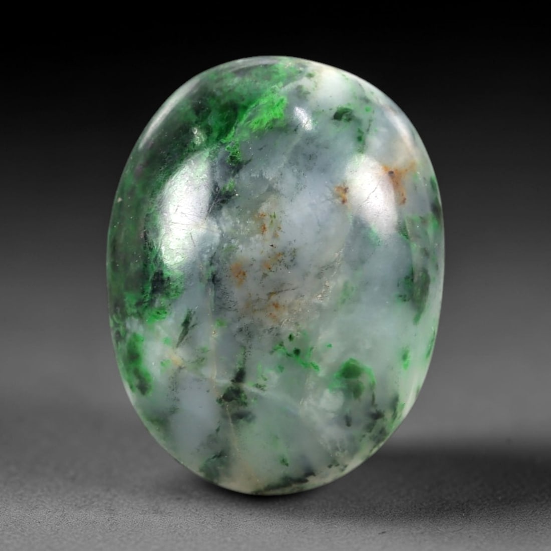 10.55 Carats Pale Matrix and Green Spot Maw Sit Sit Jade Cabochon - Natural Burmese Stone, 17AB: This maw sit sit jade cabochon is fashioned into an oval, domed form with a highly polished surface. The material exhibits a pale, semi-translucent to translucent matrix, interspersed with distinct, v