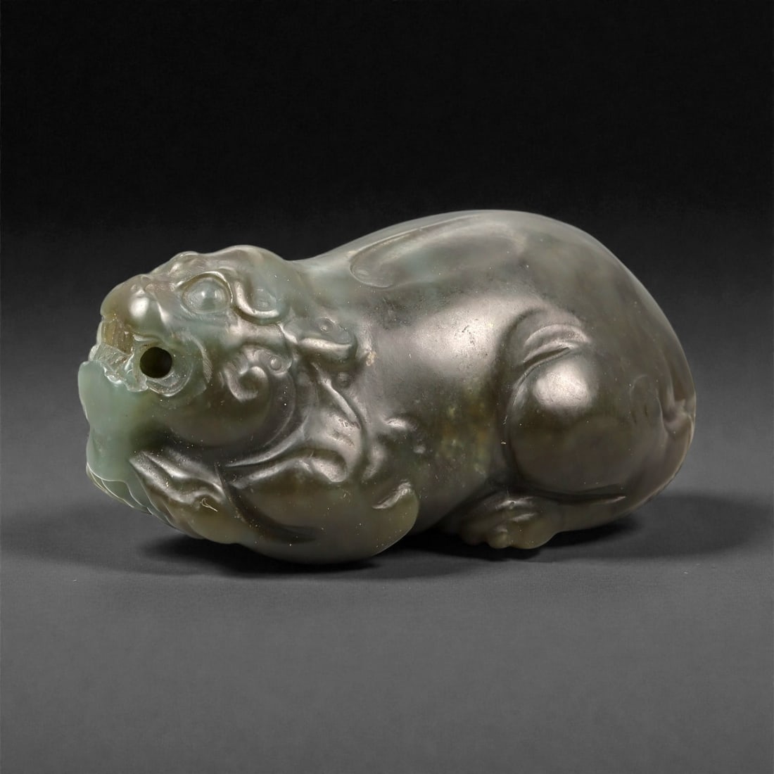 Chinese Jade Pixiu Beast - Carved Animal Figurine 5.5cm, 100ZC: Carved from green jade with areas of soft translucency and darker natural inclusions, this sculptural figure depicts a pixiu shown in a compact recumbent posture. The carving is executed fully in the