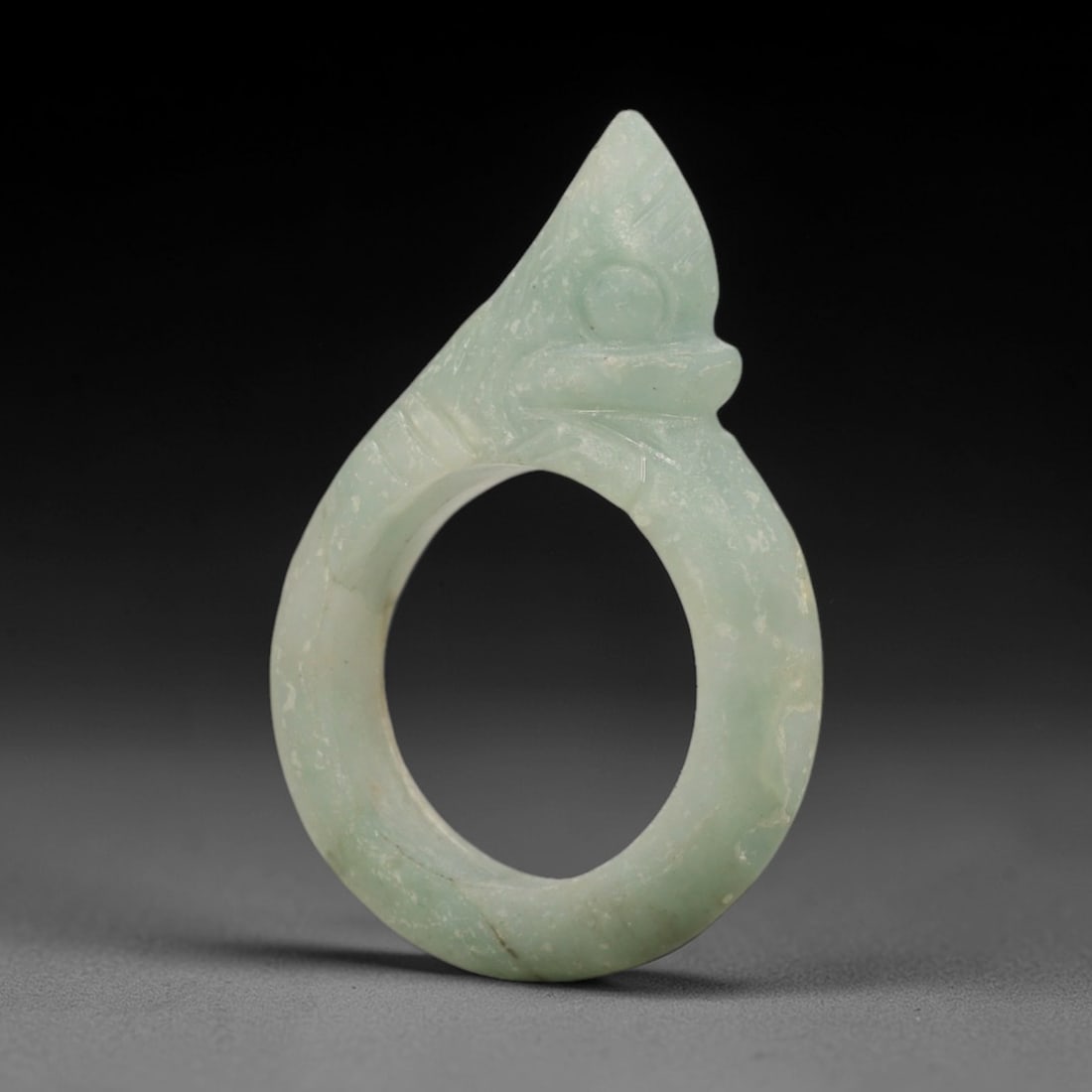 A Chinese Jadeite Jade Zoomorphic Ring, 20th Century, 11ZL: Carved from pale green jadeite with a matte to lightly polished surface, the object is formed as a finger ring with an integrated zoomorphic terminal, likely representing a stylized bird or beast head