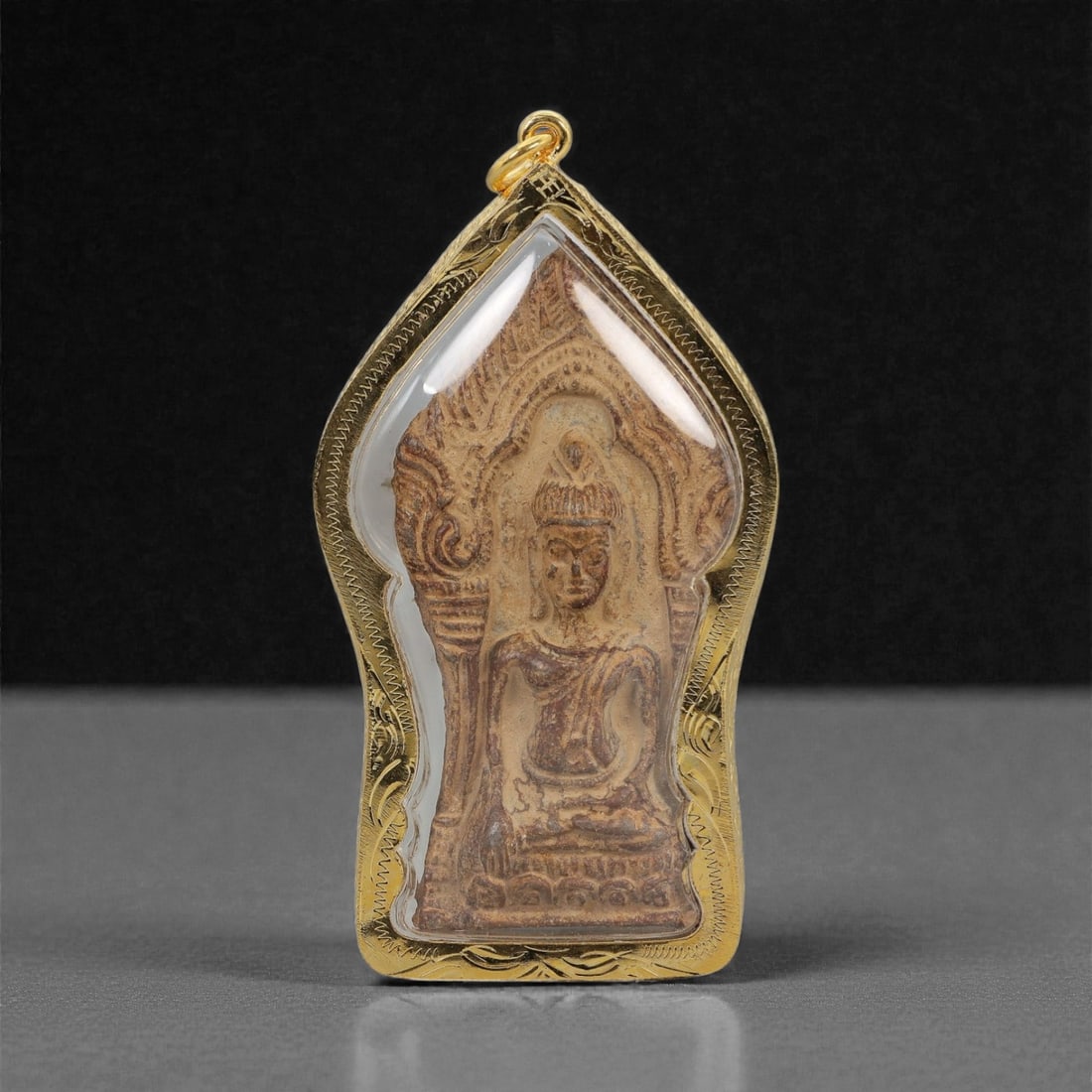 A Thai Buddhist Composite Amulet in Gilt Metal Frame, 20th Century, 59FN: The amulet is encased in a gilt metal frame of stylized arched form with a suspension loop at the apex and fine incised border detailing. The obverse features a composite plaque of compressed organic
