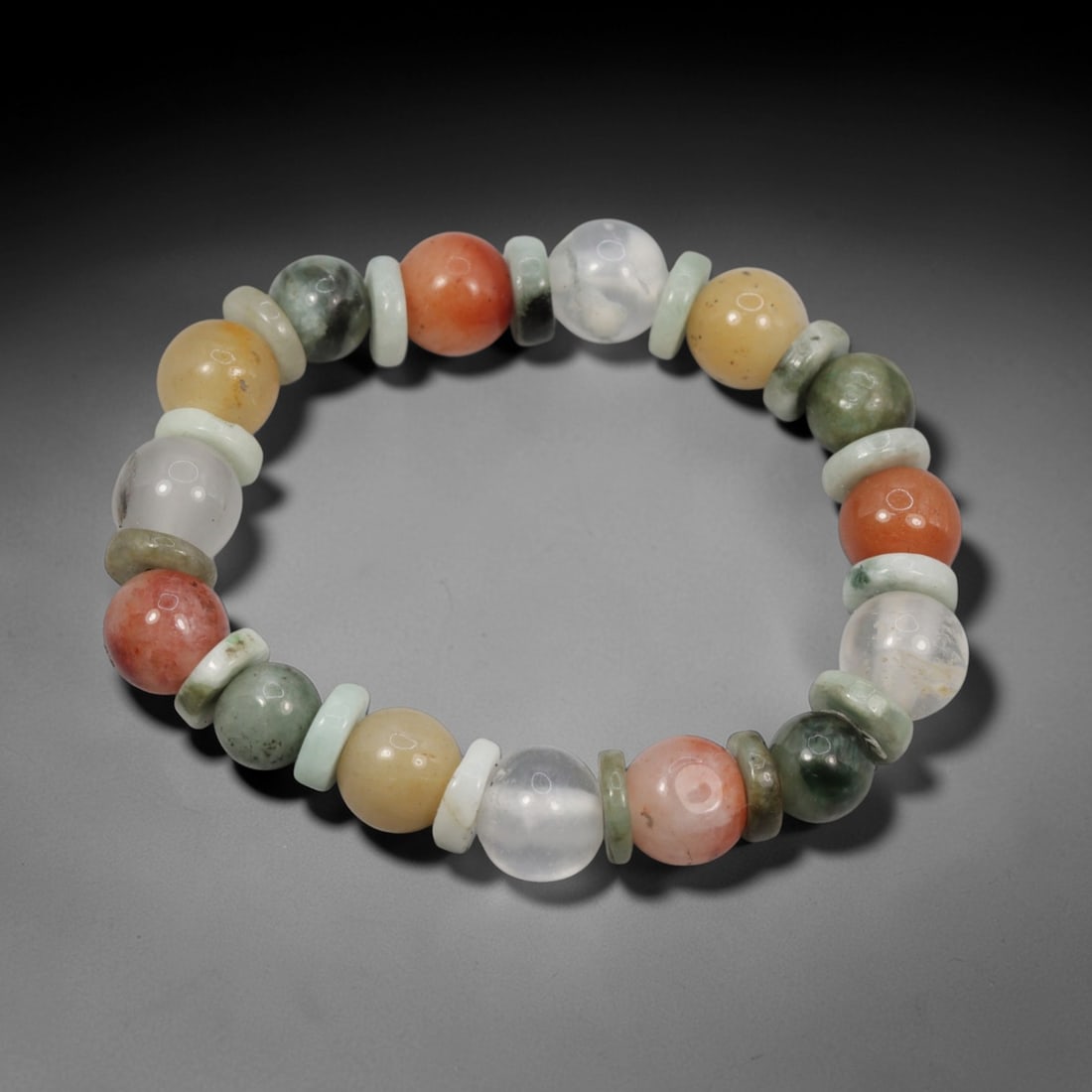 A Chinese Quartz and Jadeite Jade Bead Bracelet, 20th Century, 43ZK: Strung with spherical beads of quartz and jadeite jade, separated by flat disc-shaped spacers. The quartz beads display a spectrum of natural hues, including clear, pale yellow, orange, and reddish-pi