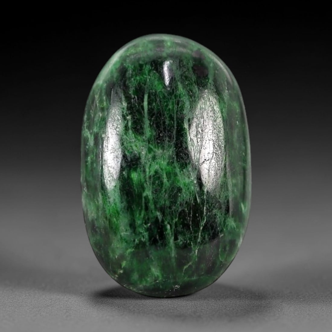 4.28 Carats Deep Green Maw Sit Sit Jade Cabochon - Natural Burmese Stone, 7AB: This maw sit sit jade cabochon is fashioned into an oval, domed form with a highly polished surface. The material exhibits a deep, saturated green matrix, interspersed with distinct, lighter green vei