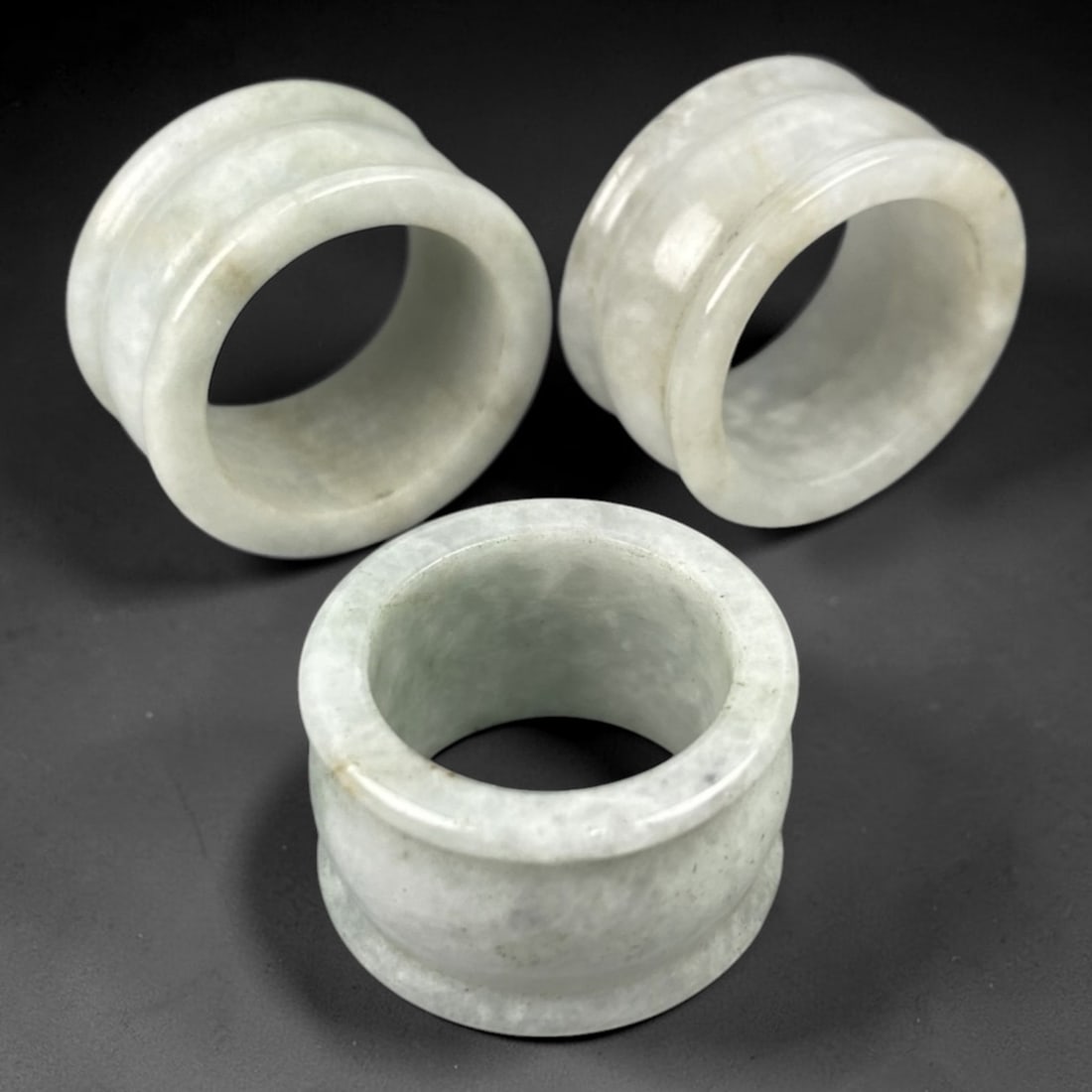 A Trio of Chinese Jade Archer Rings - 20th Century, 97FW: Crafted from pale celadon jade with subtle mineral inclusions, this set of three archer rings features thick cylindrical forms with raised double collars at both ends, characteristic of traditional Ch