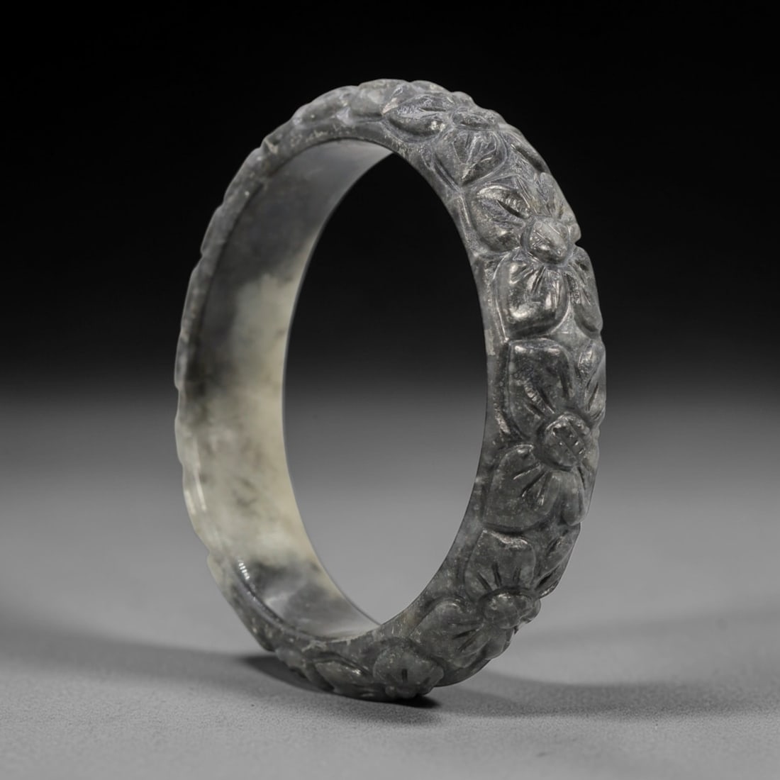 A Chinese Carved Jadeite Jade Bangle Bracelet, 20th Century, 47ZL: A fine jadeite bangle of flattened circular form, masterfully carved in relief with a continuous band of floral blossoms and scrolling foliate motifs. The stone exhibits a striking variegated palette,